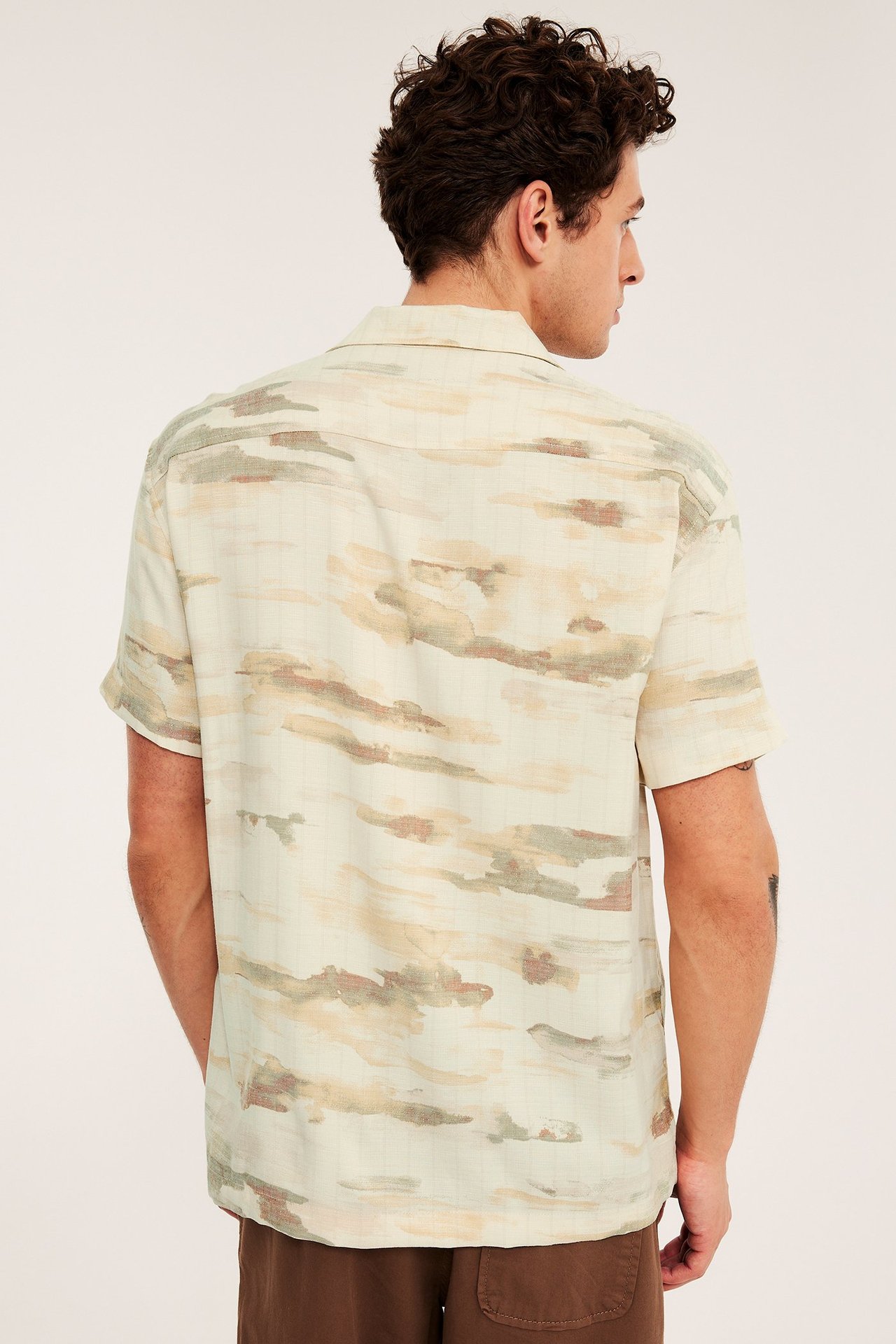 Bakifrån på en man i en beige mönstrad kortärmad resortsjorta och bruna shorts.