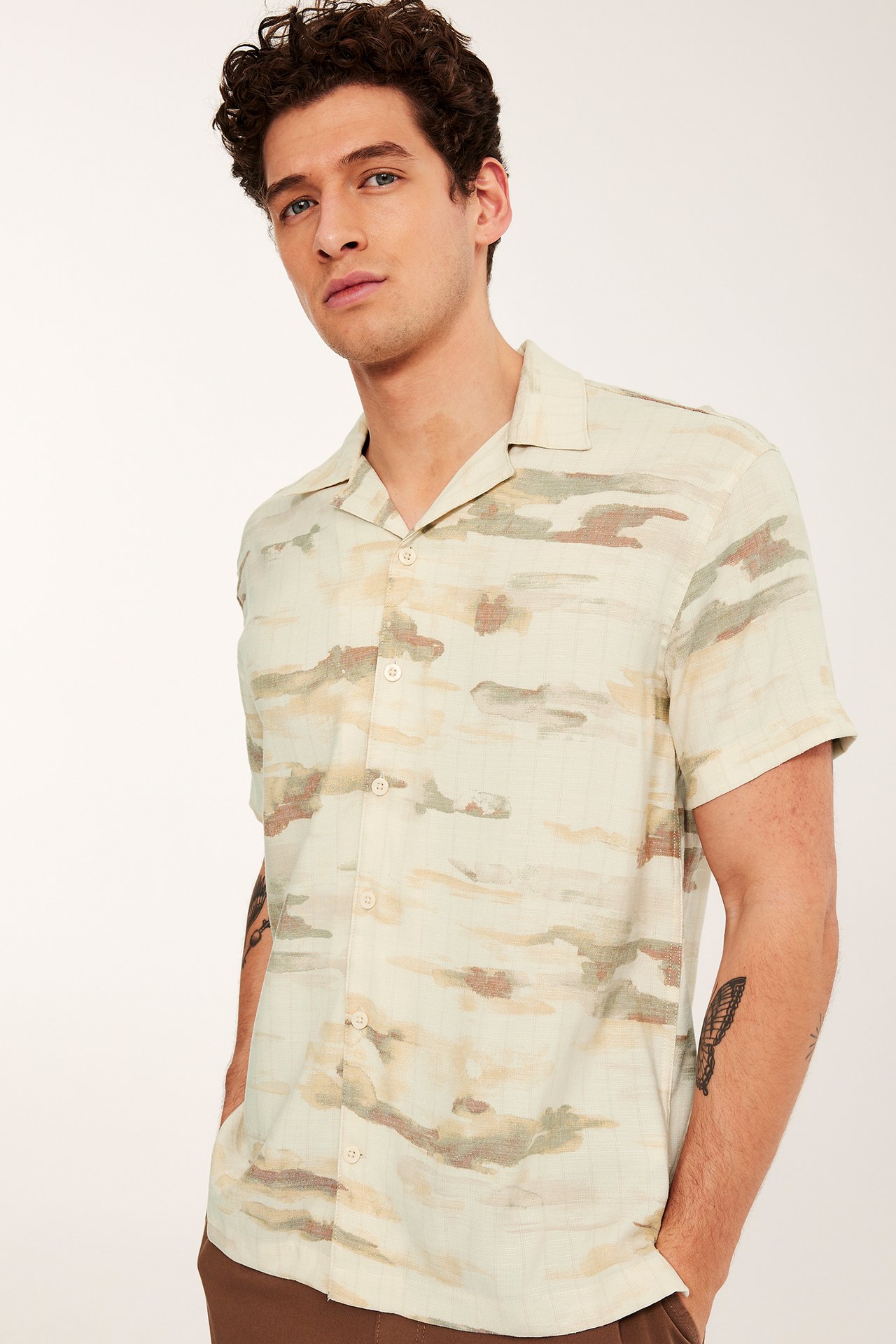 Forfra, en mann i en beige mønstret kortermet resortskjorte med knapper.
