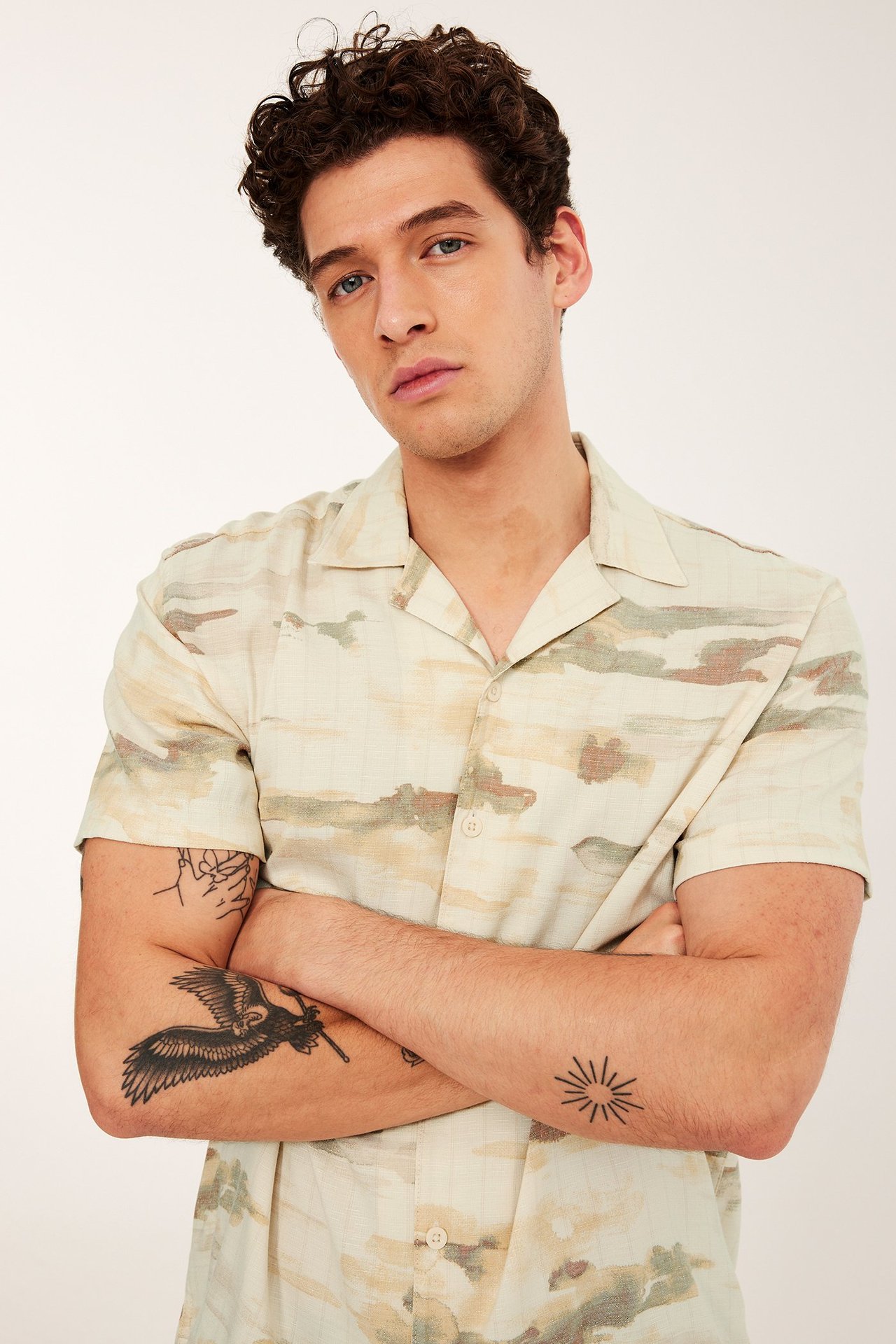 Framifrån, en man i en beige kortärmad resortskjorta i viskosmix med abstrakt mönster.