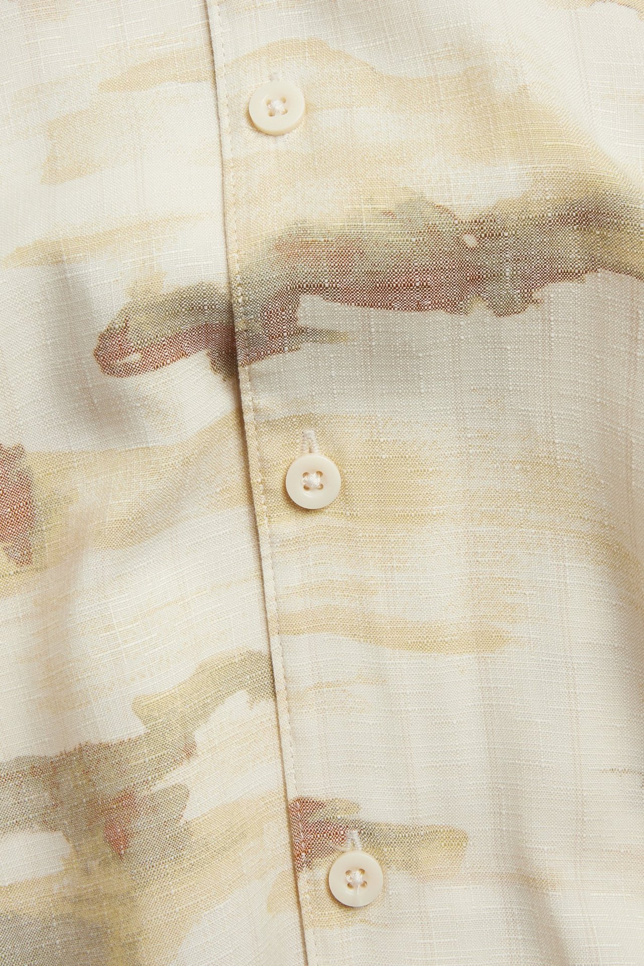 Närbild på en beige mönstrad kortärmad skjorta i polyester-viskosmix med knappar fram.
