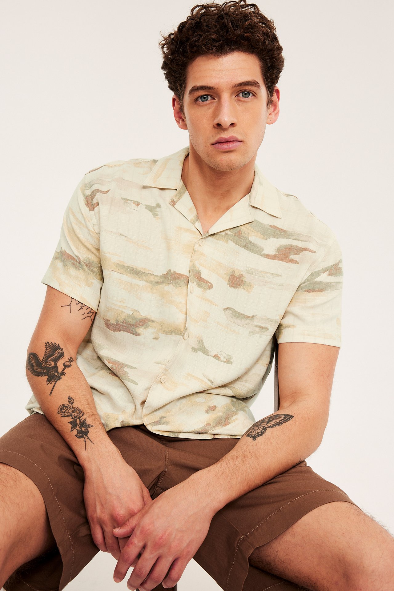 Frontbilde av en mann i en beige mønstret kortermet resortsjorte og brune shorts.