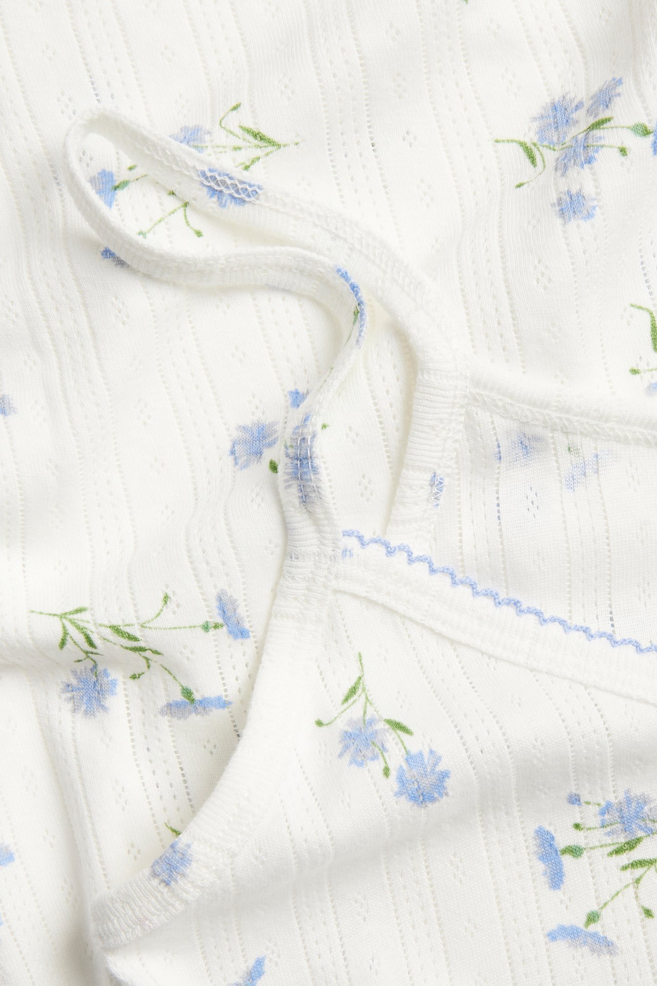 Zbliżenie białej bawełnianej koszuli nocnej pointelle w jasnoniebieski kwiatowy wzór, z cienkimi ramiączkami i falbanką.