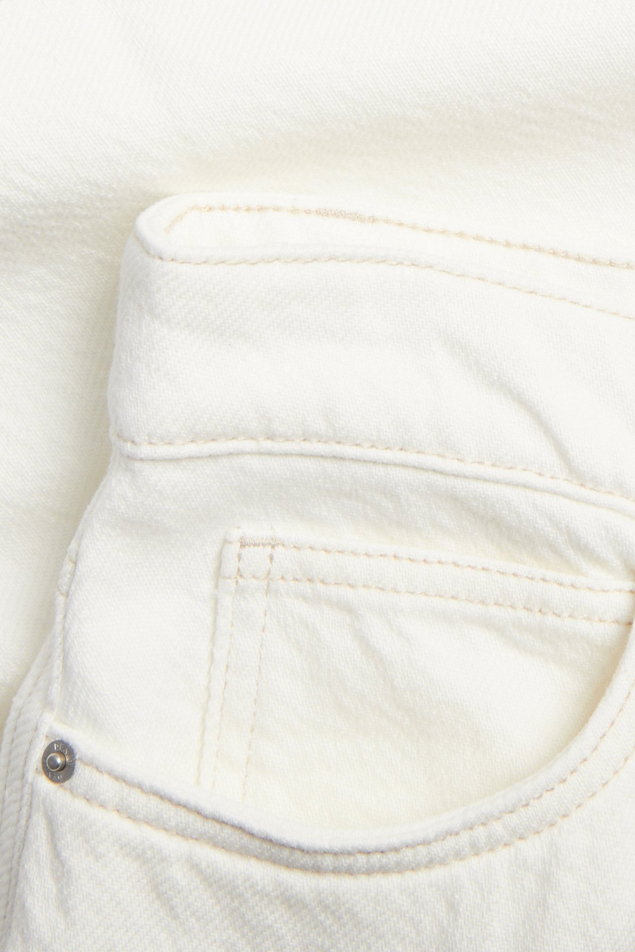 Nærbilde av et off-white bomullstwillskjørt med frontlomme og nagledetalj.