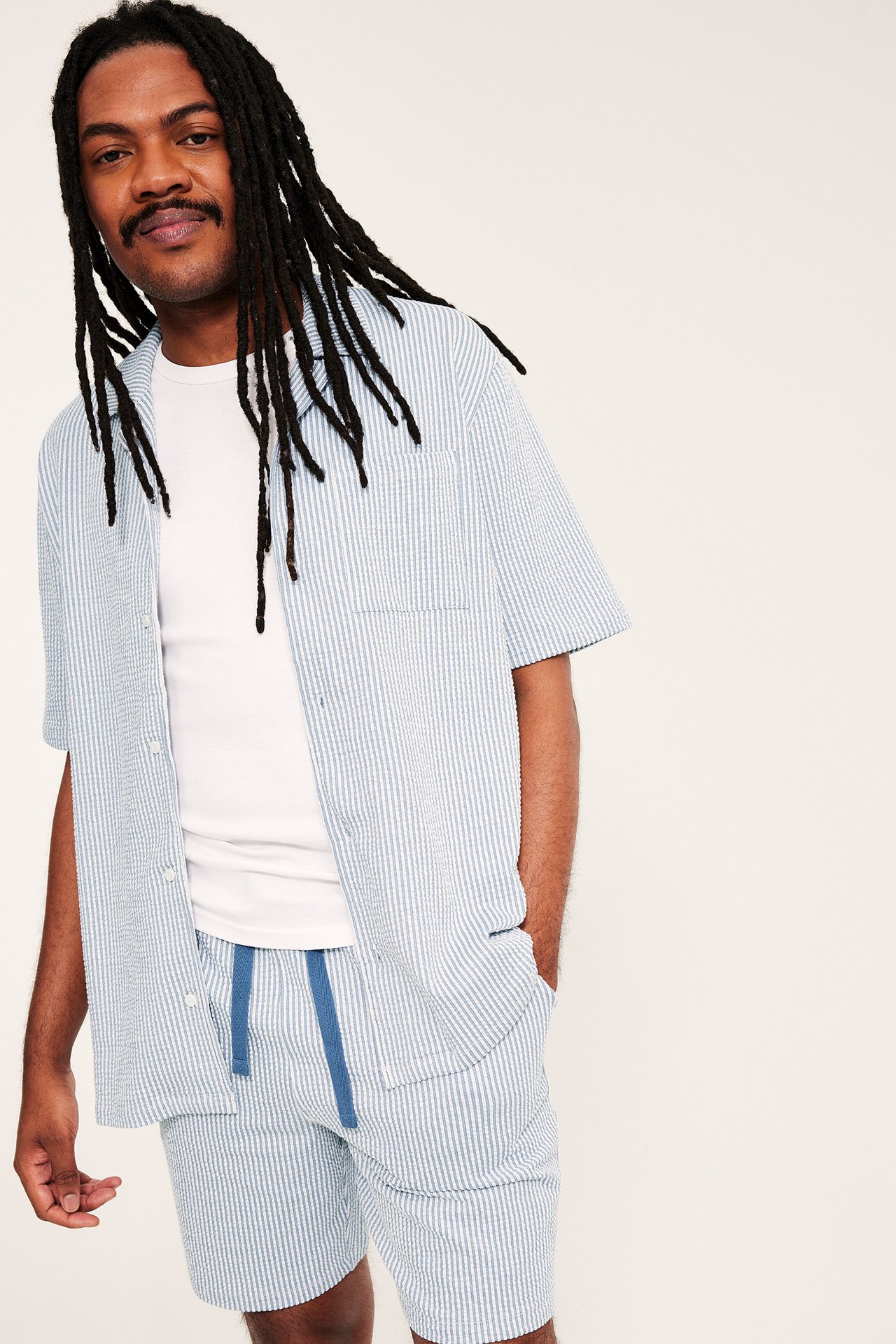 Edestä, mies yllään vaaleansinivalkoraidalliset seersucker-pyjamashortsit ja yhteensopiva avoin lyhythihainen paita.