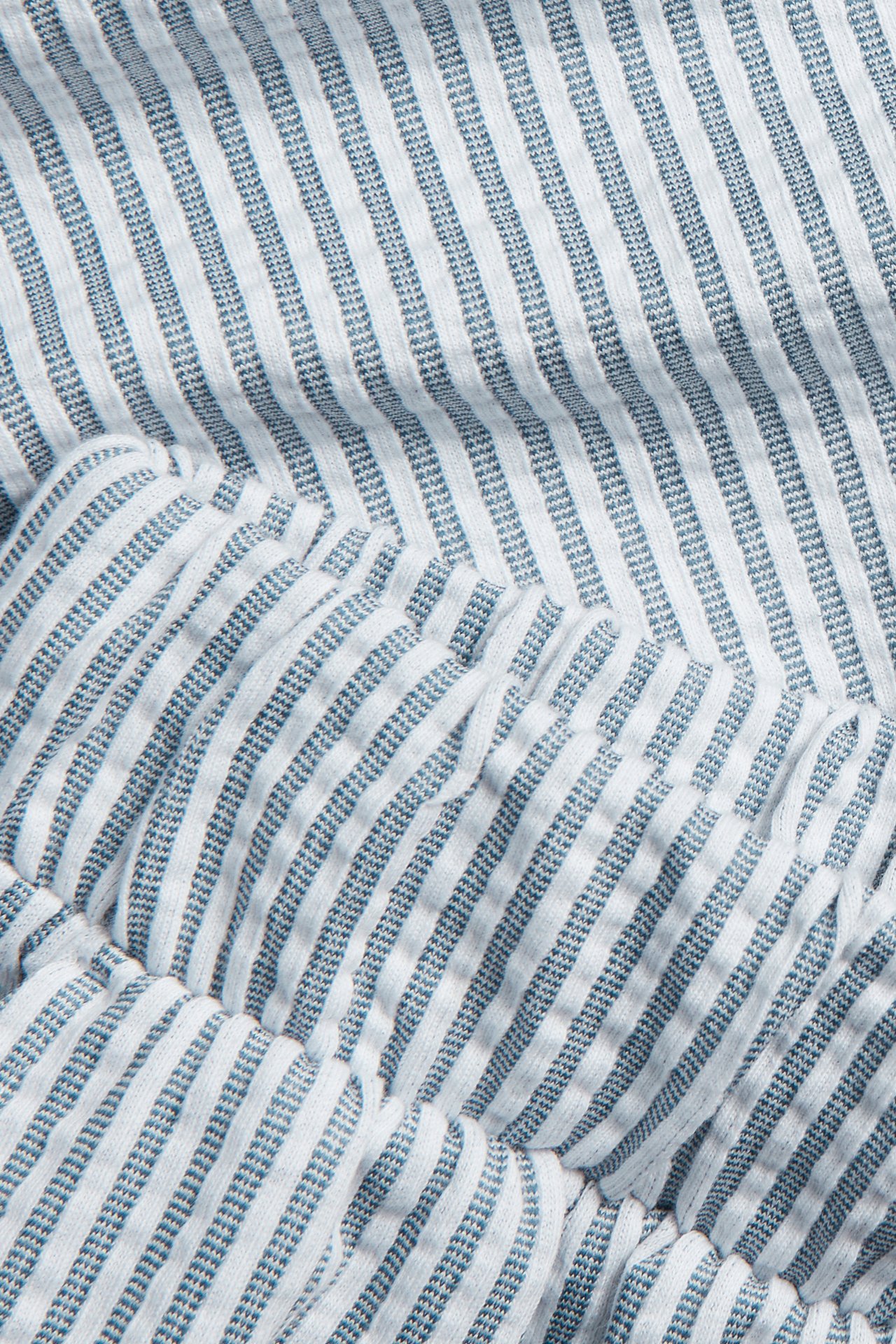 Lähikuva tummansinisistä ja valkoisista raidallisista seersucker-trikoopäiväunishortseista, joissa on joustava yksityiskohta.