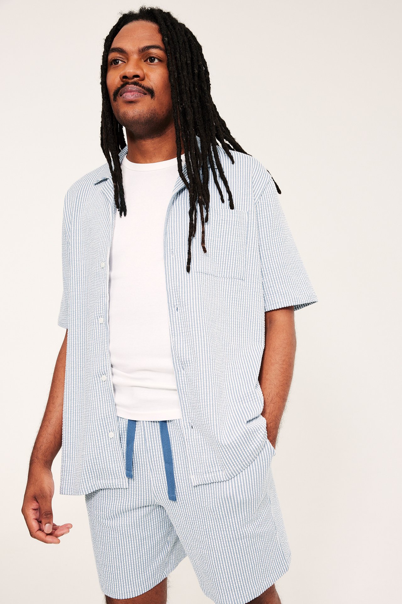 Mies yllään vaaleansiniraidalliset seersucker-pyjamashortsit kiristysnauhalla, yhteensopiva paita ja valkoinen t-paita.