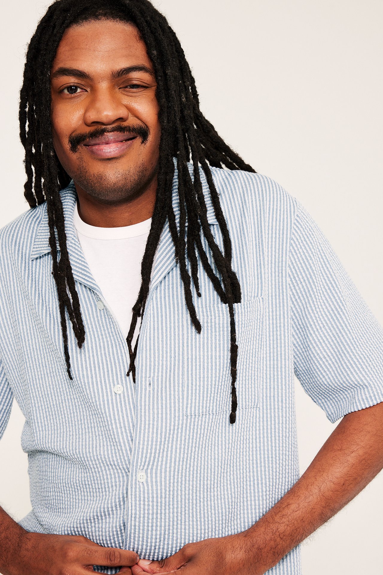 Lähikuva edestä miehestä yllään vaaleansininen raidallinen seersucker-pyjamapaita resort-kauluksella ja rintataskulla.