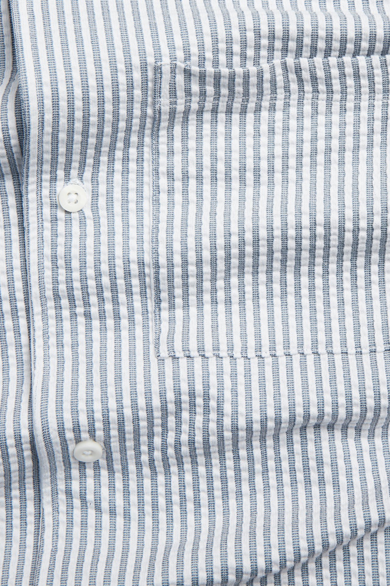 Nærbilde av en mørkeblå- og hvitstripet seersucker pyjamasskjorte for menn med brystlomme og hvite knapper.