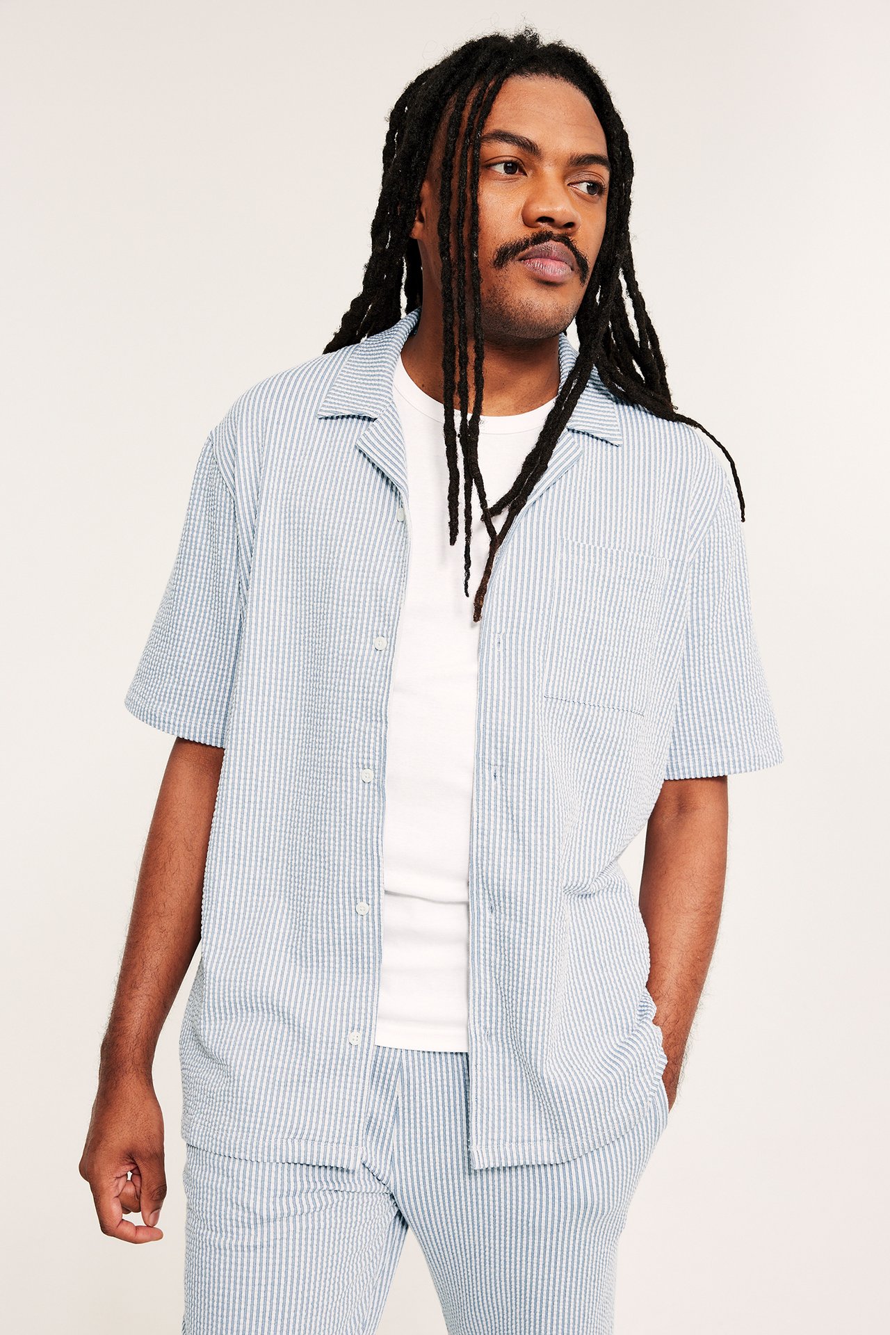 Edestäpäin: mies yllään vaaleansininen raidallinen seersucker-pyjamapaita, valkoisen t-paidan ja yhteensopivien housujen päällä.