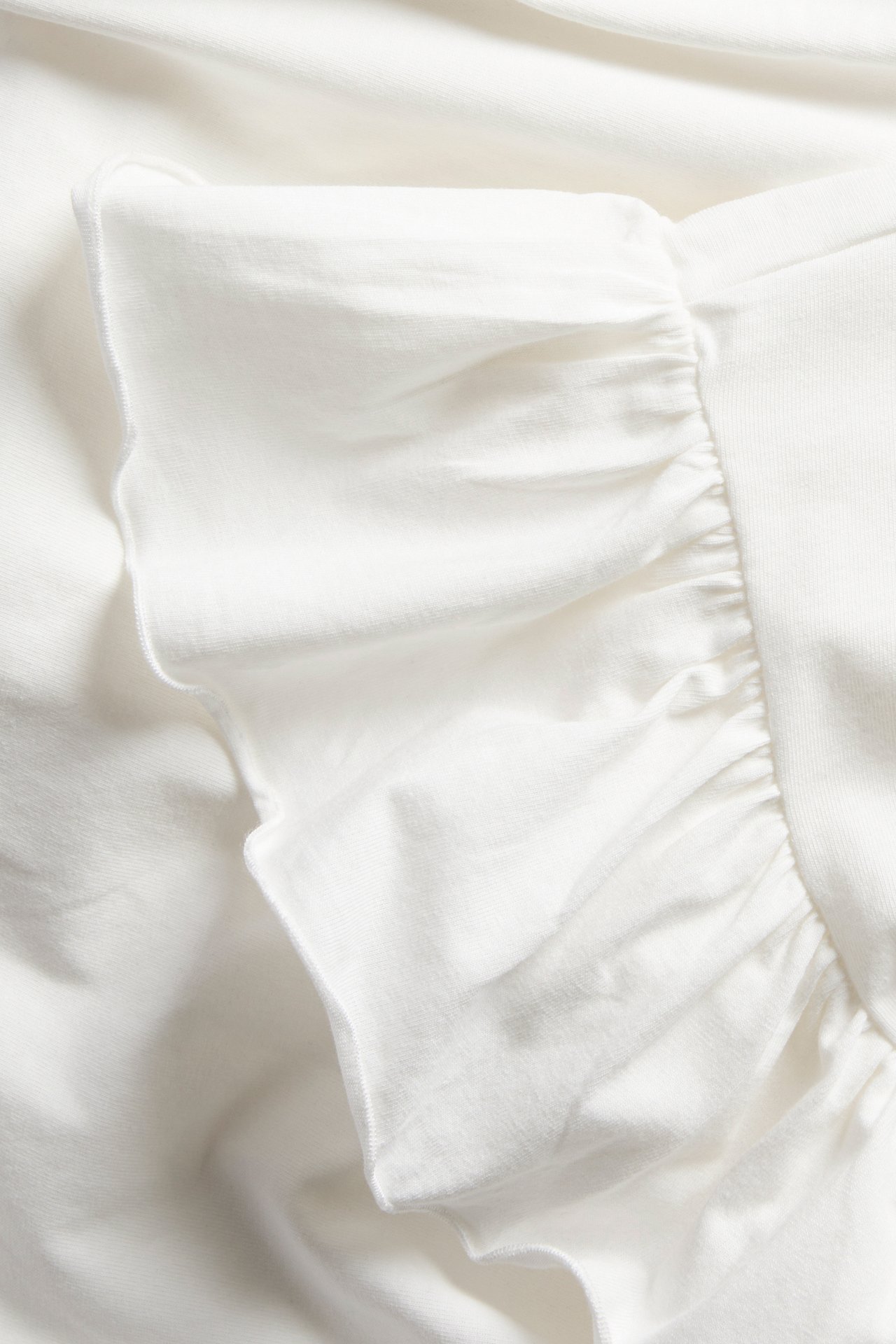 Närbild av offwhite kortärmad topp i bomullsjersey med volangärm.