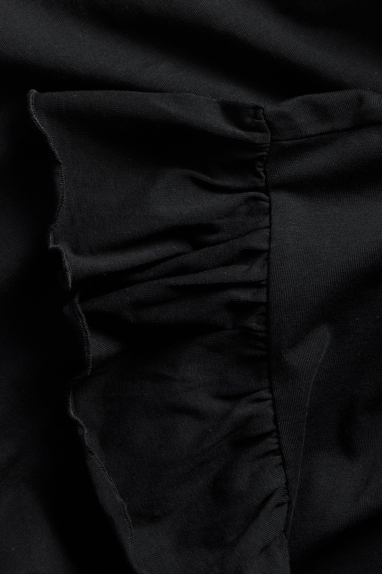 Närbild av en svart topp i bomullsjersey med volangärmdetalj.