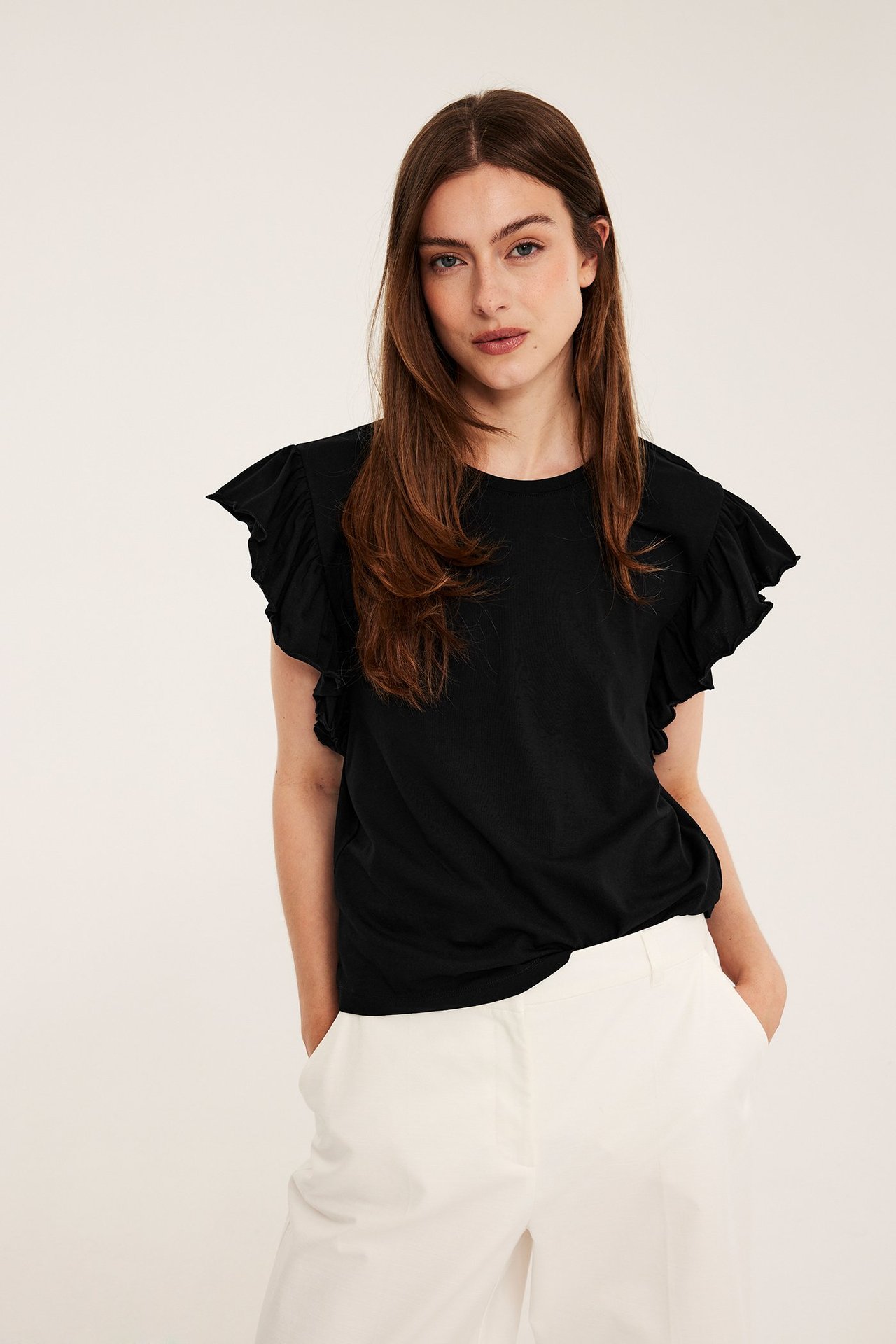 Framsida av kvinna i svart kortärmad bomullsjerseytopp med volangärm och vita byxor.