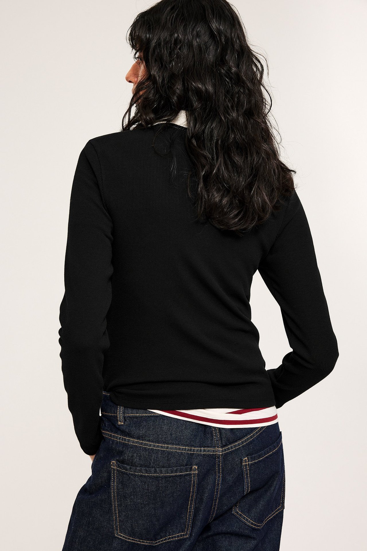 Takaa: Nainen mustassa ribbineuleisessa pitkähihaisessa topissa, valkoisen raidallisen toppi ja tummansiniset farkut.