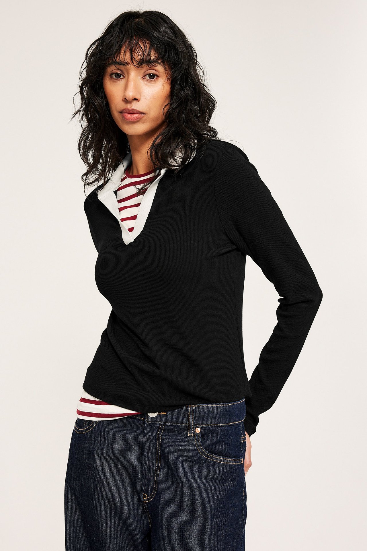 Etukuva: Nainen yllään musta ribattu pitkähihainen paita valkoisella kauluksella, raidallisen paidan ja tummansinisten farkkujen päällä.