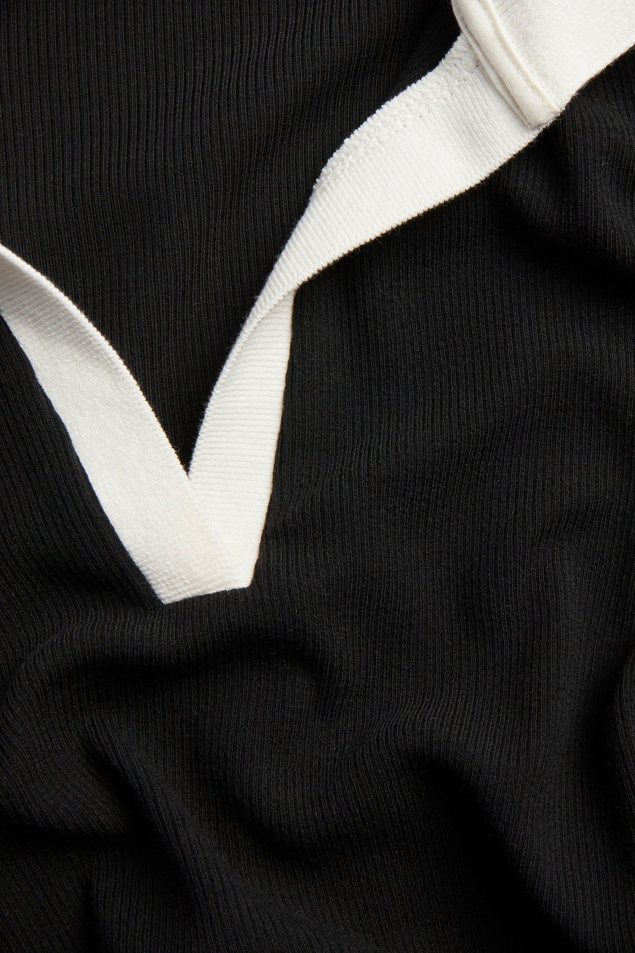 Lähikuva mustasta istuvasta ribbineuleisesta pitkähihaisesta topista valkoisella V-pääntiellä.