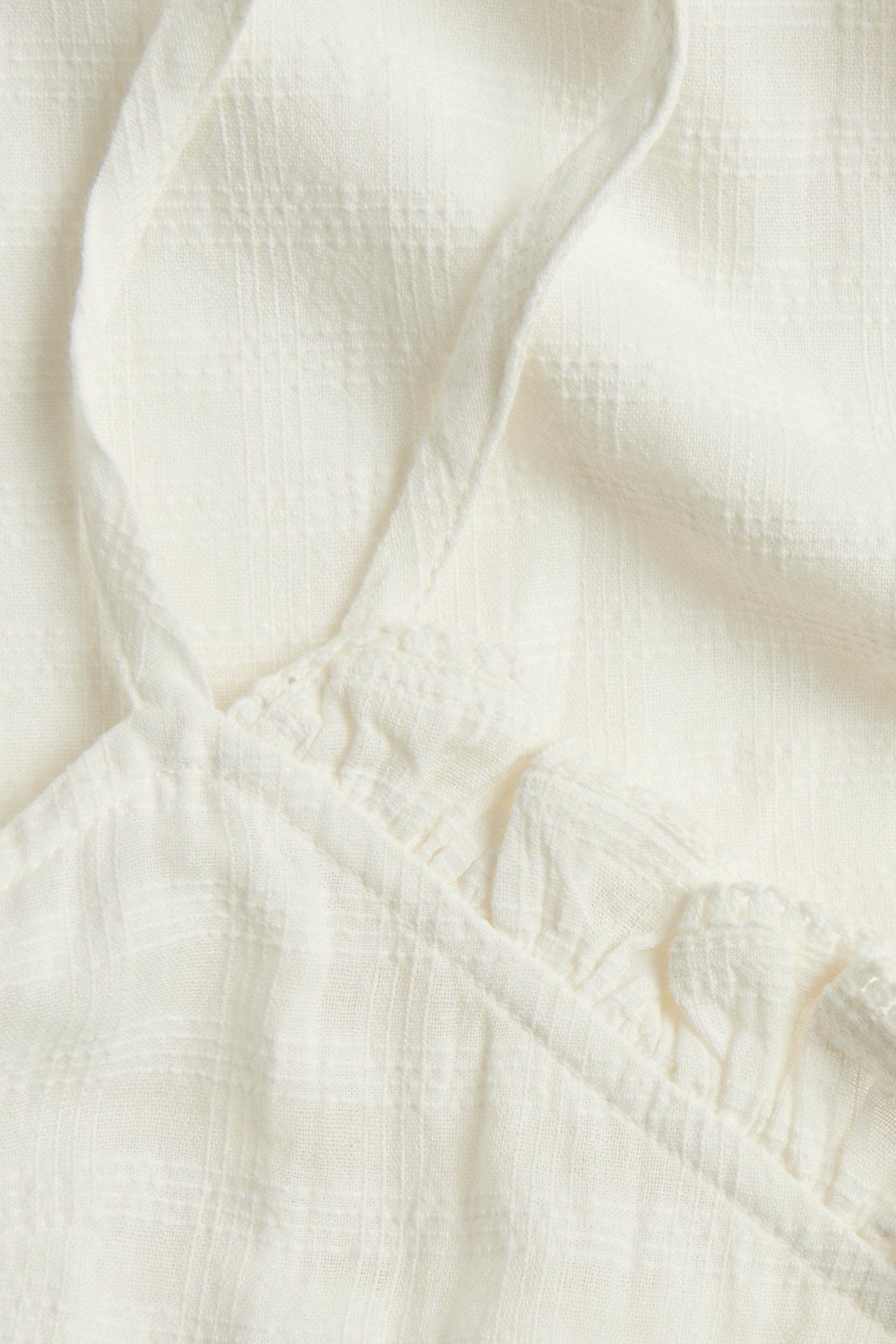 Nærbilde av en offwhite vevd bomulls-nattkjole med strukturmønster, regulerbar stropp og volang.