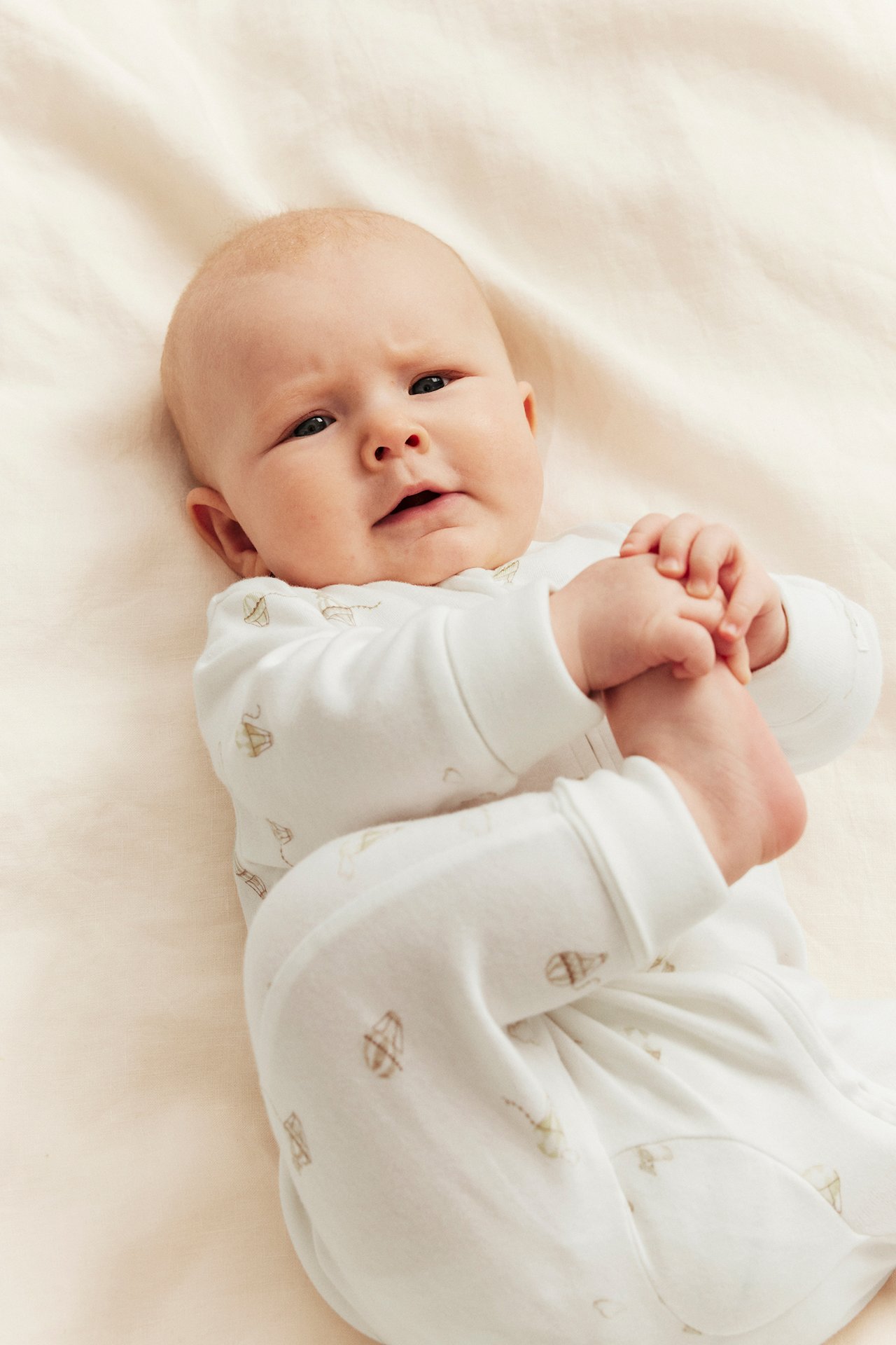 Forfra: Baby i offwhite bomullsromper med luftballongmønster og glidelås foran.