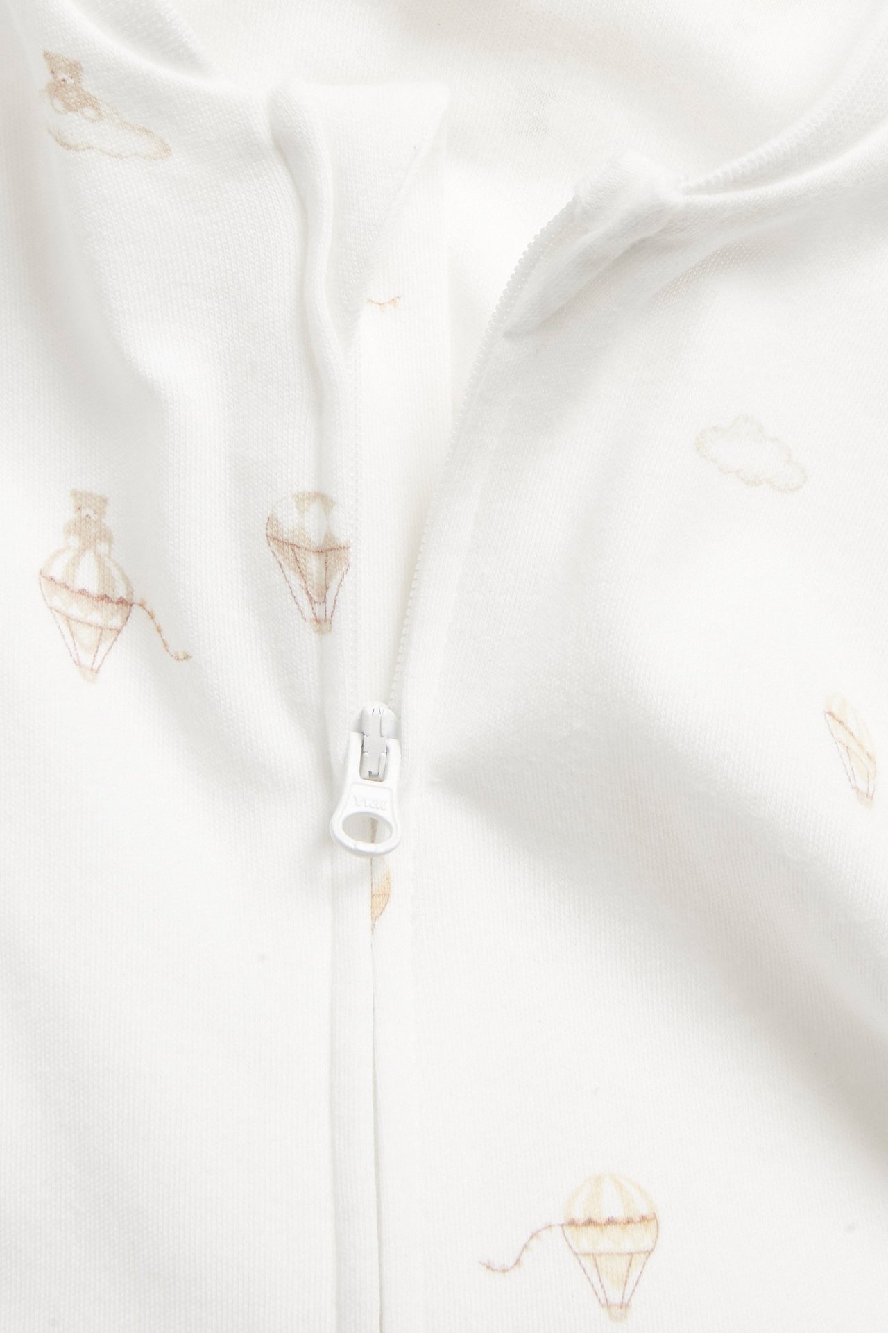 Zbliżenie na ecru pajacyk niemowlęcy z jasnobrązowym wzorem balonów i zamkiem z przodu.