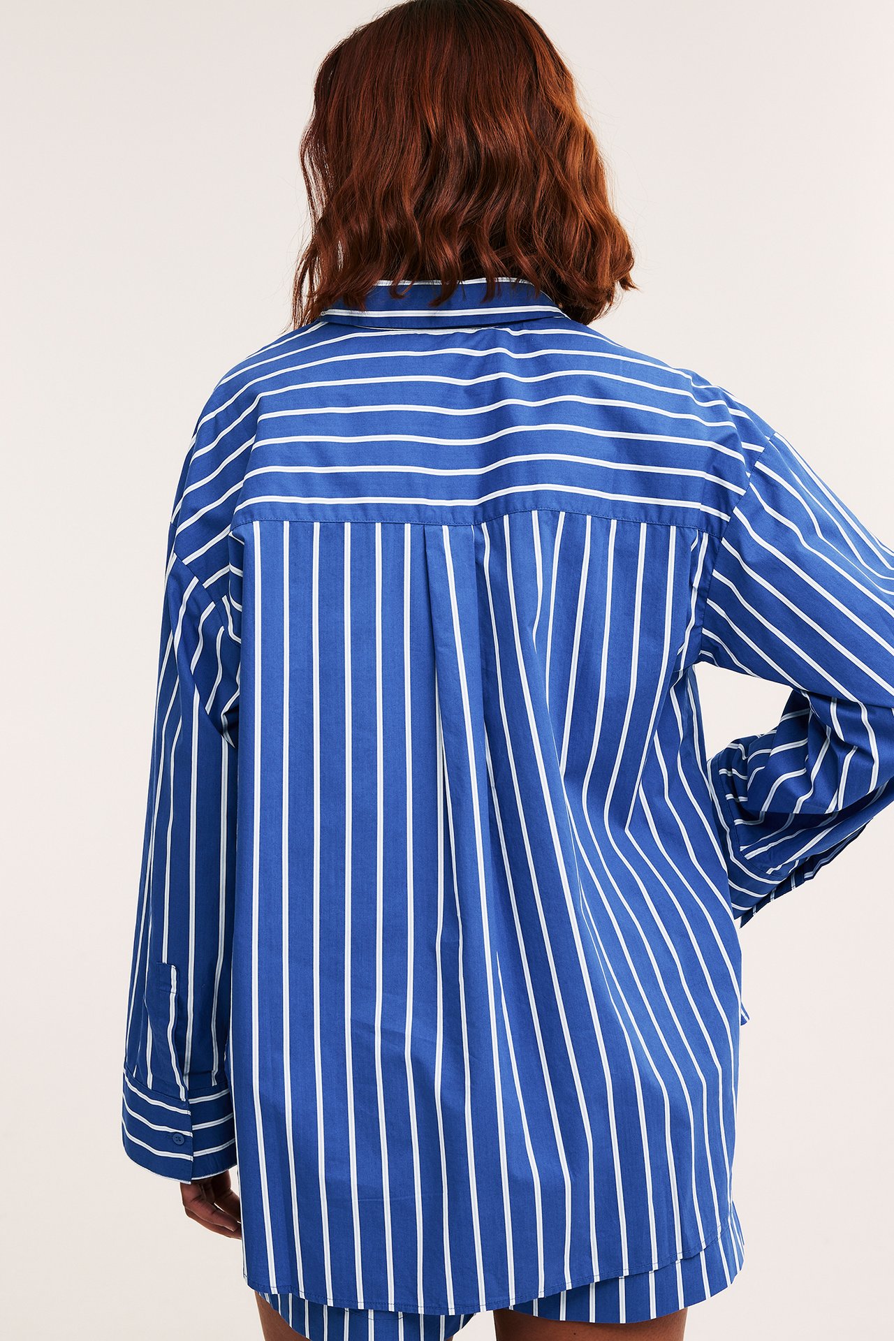 Ryggvisning av kvinne i en oversized blå- og hvitstripet bomullspoplinskjorte.