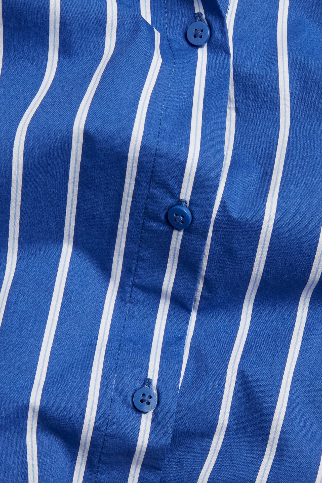 Zbliżenie niebiesko-białej koszuli popelinowej w paski, z niebieskimi guzikami na plisie.