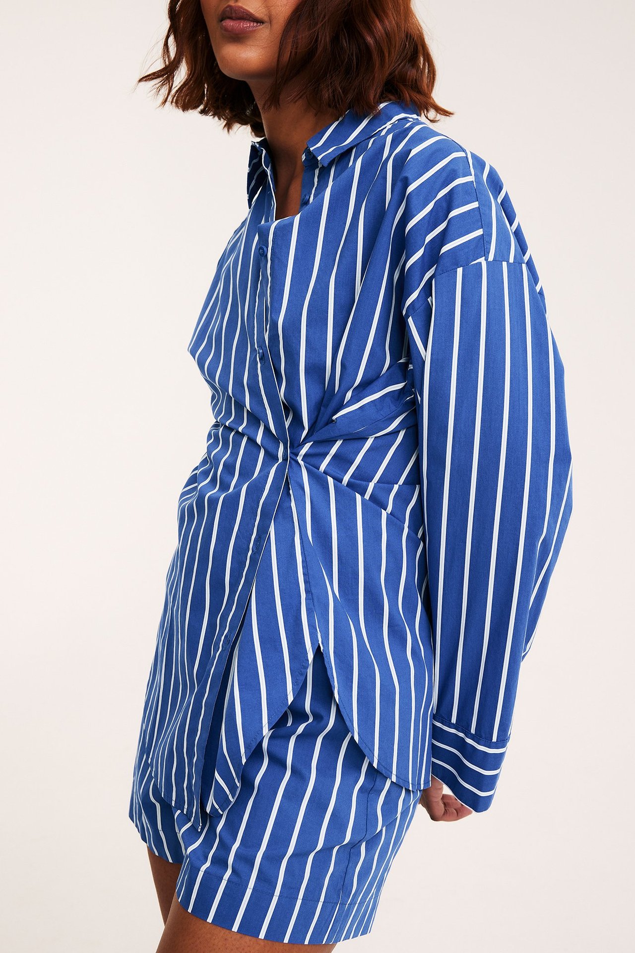 Front: kvinne i blå og hvit stripet poplinskjorte med vridd front og matchende shorts.
