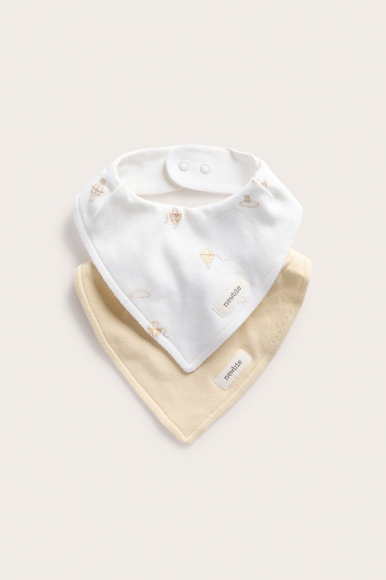 Widok z przodu: Dwa śliniaki. Jeden kremowy w balony, drugi jasnożółty, oba zapinane na zatrzaski.