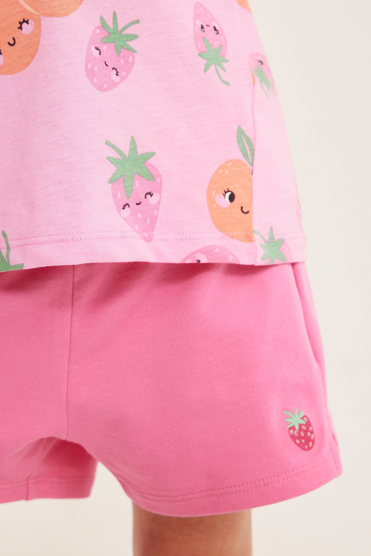 Nærbilde, forfra, av rosa bomullsshorts for barn med jordbroderi og en rosa topp med fruktmønster.