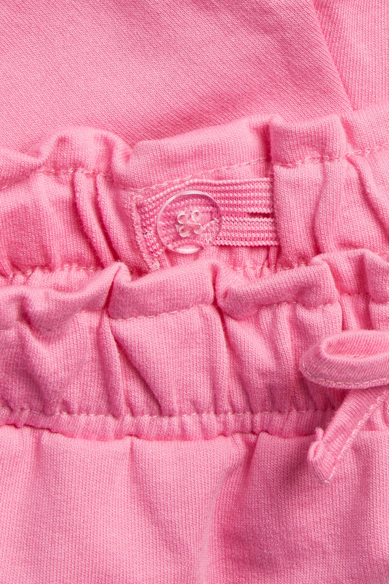 Nærbilde av rosa barneshorts i bomull med justerbar elastisk linning og gjennomsiktig plastknapp.