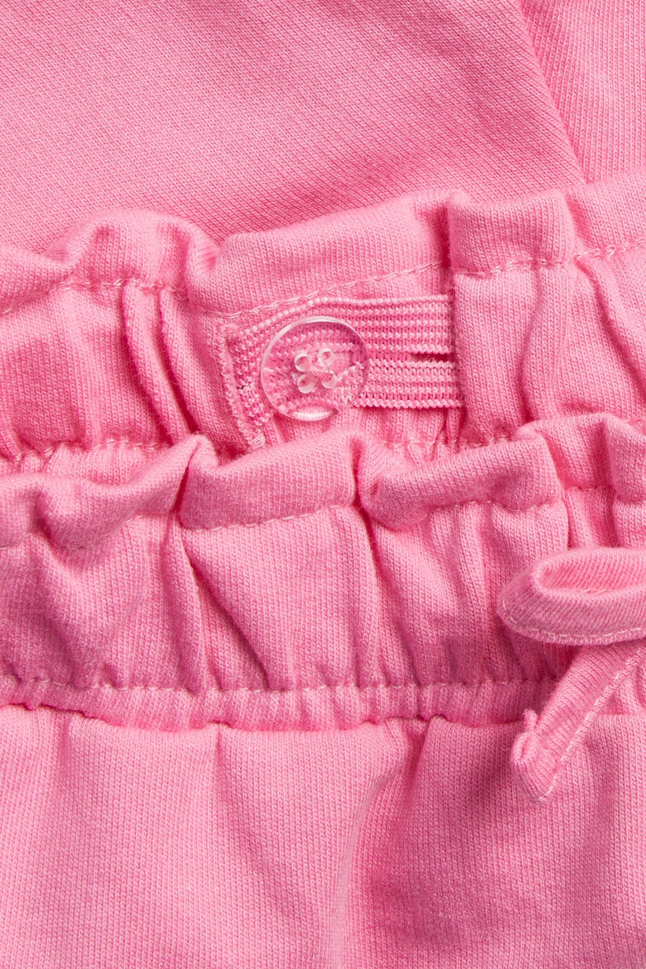 Zbliżenie różowych szortów dziecięcych z bawełny, z regulowaną elastyczną talią i przezroczystym guzikiem.