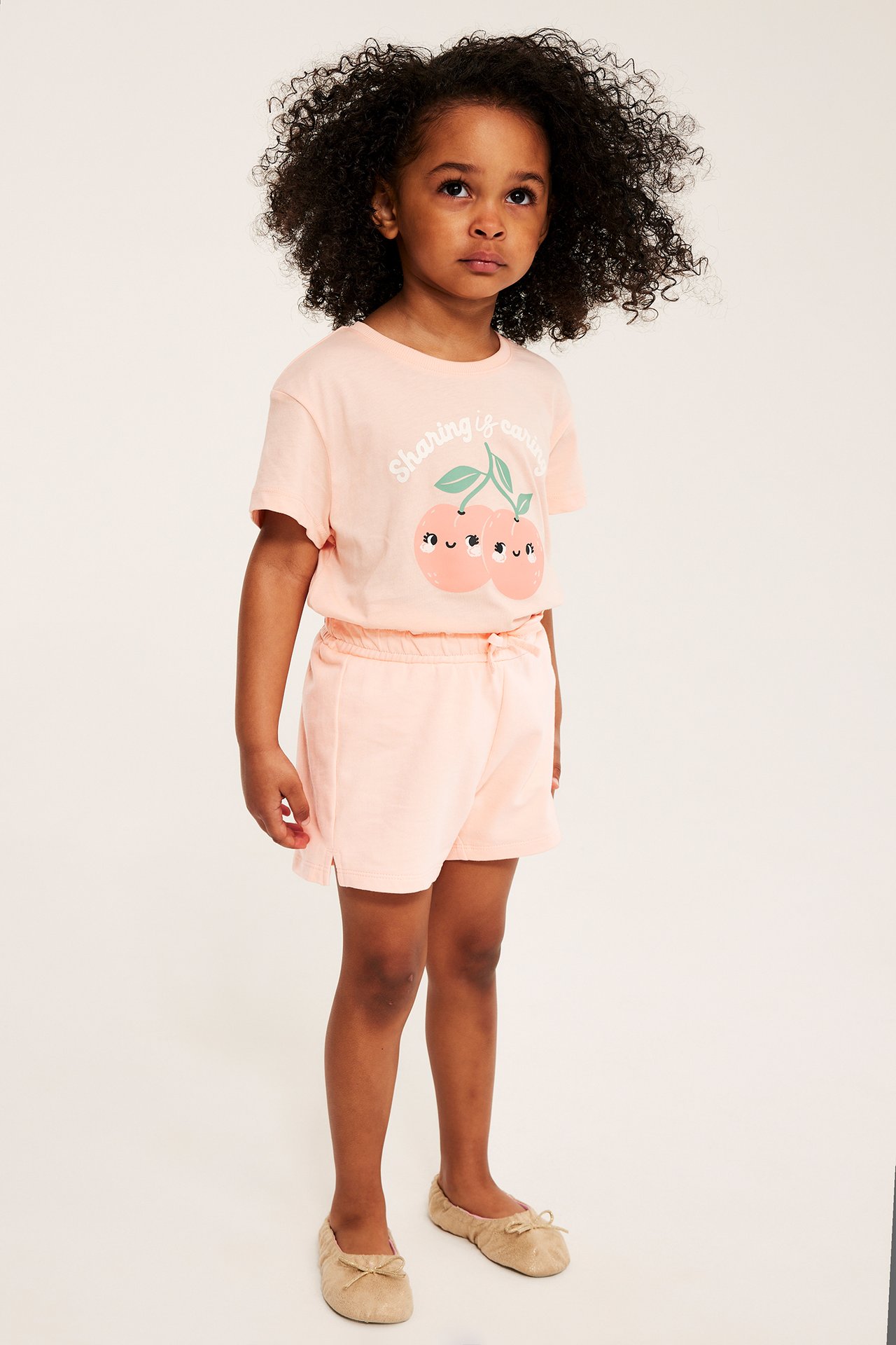 Framsida: barn i ljusrosa bomullsshorts och en ljusrosa t-shirt med körsbärstryck.