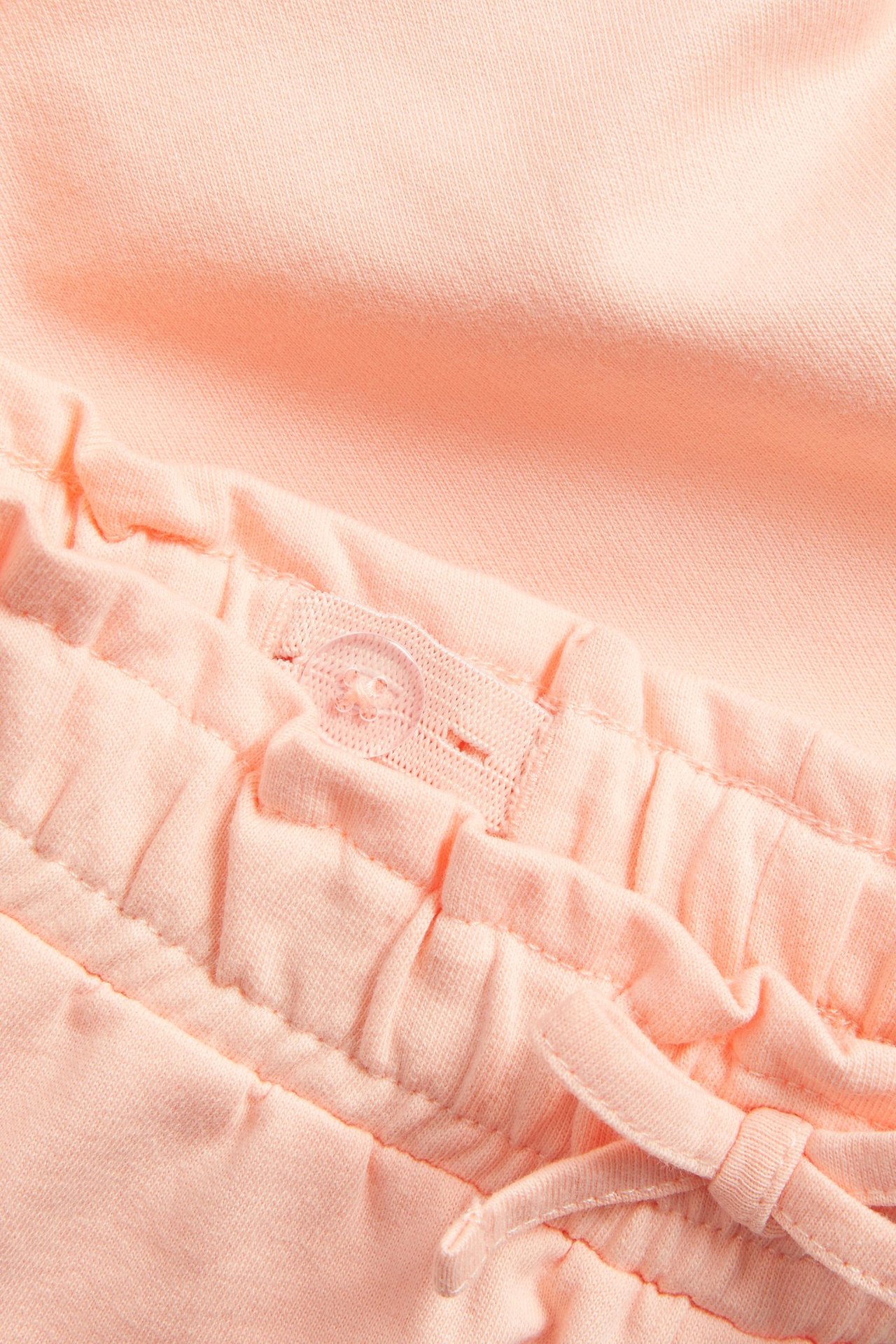 Zbliżenie koralowych bawełnianych szortów z elastycznym pasem, regulowanym guzikiem i ozdobnym wiązaniem.