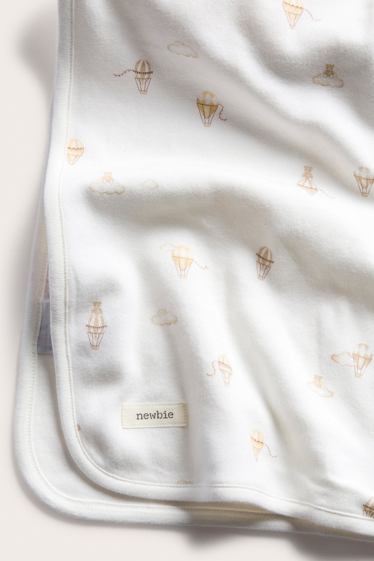 Zbliżenie na kremowobiały kocyk niemowlęcy z bawełny z wzorem w balony na ogrzane powietrze i chmury.