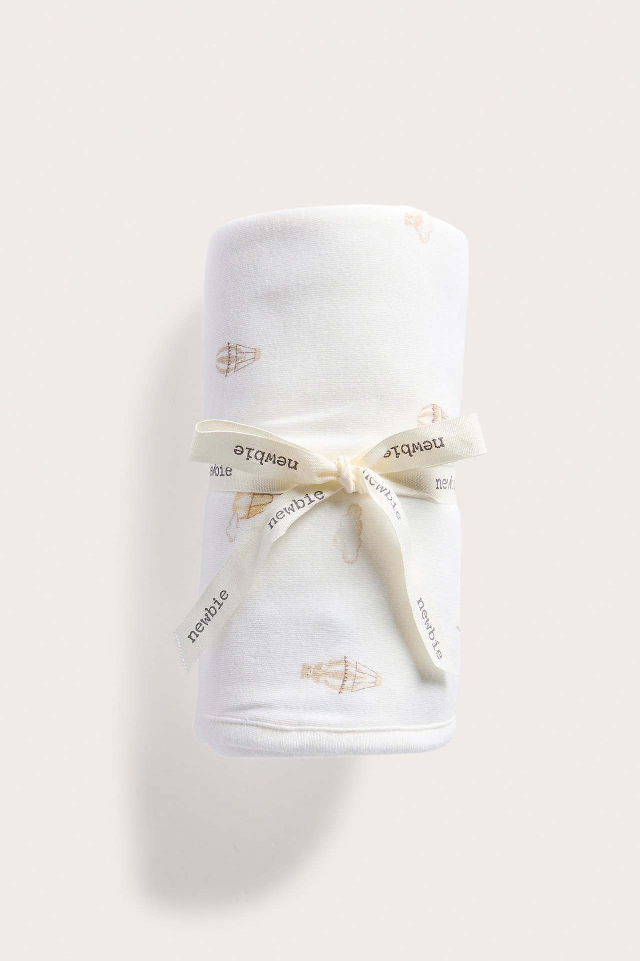 Widok z przodu kremowego kocyka dziecięcego z bawełny z wzorem balonów, przewiązanego kremową wstążką.