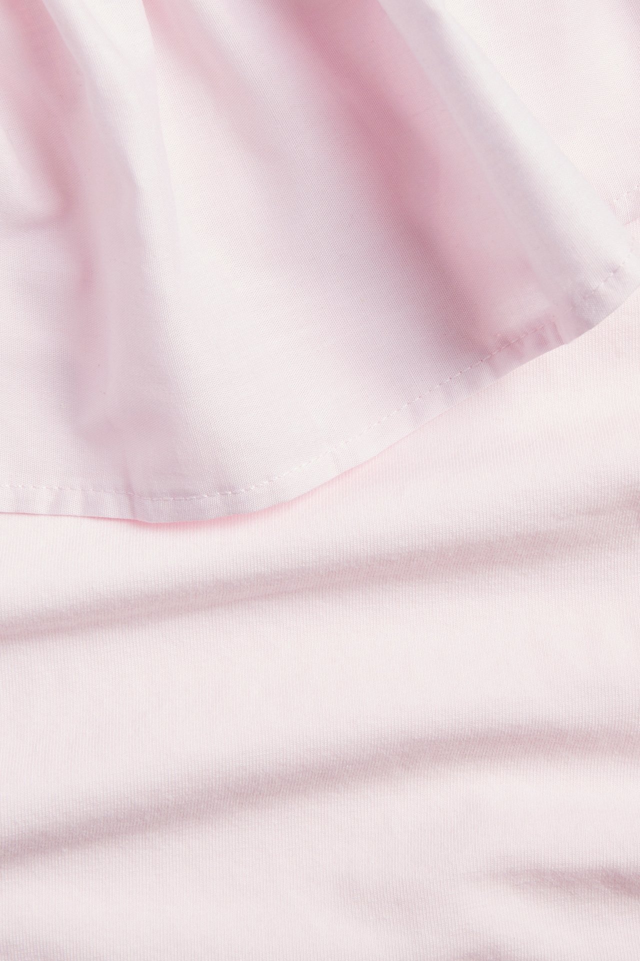 Zbliżenie na jasnoróżowy, jednokolorowy bawełniany top z jednym ramieniem i falbanką, ukazujące tkaninę.
