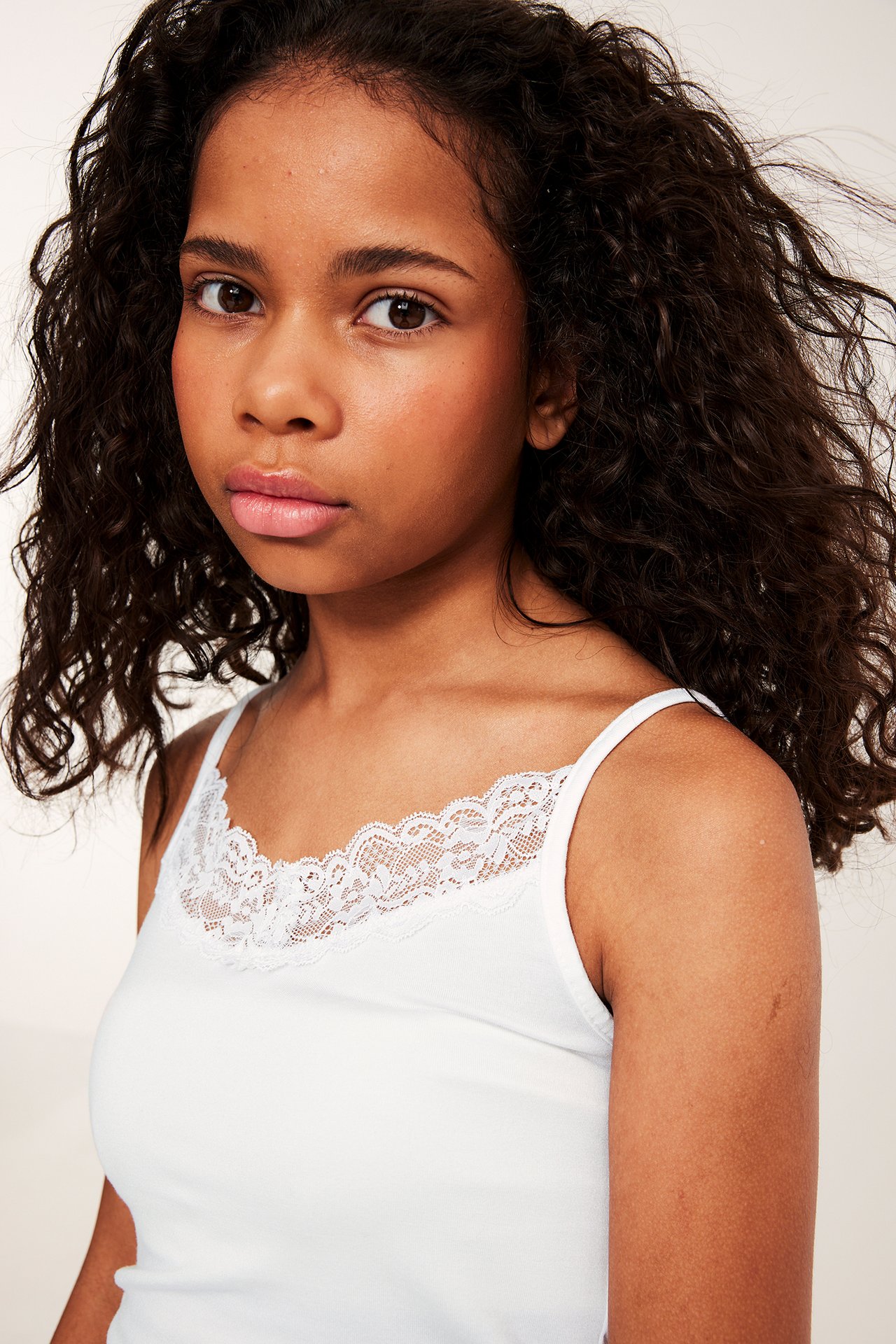 Lähikuva, edestä, lapsi yllään valkoinen toppi, jossa herkkä pitsireunus pääntien ympärillä.