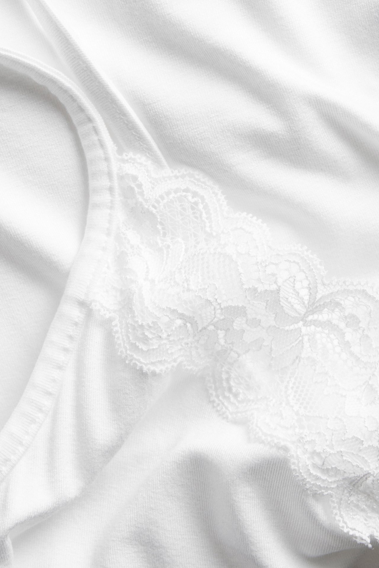 Lähikuva valkoisesta aluspaidasta, jossa on herkkä valkoinen pitsireuna pääntiessä.