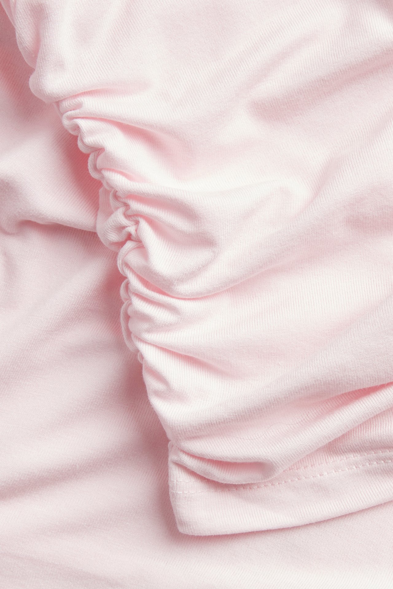 Närbild av en ljusrosa draperad topp i viskos-elastan med tydliga rynkade detaljer.
