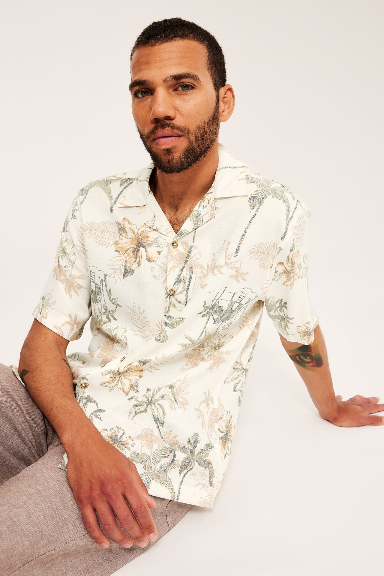 Framifrån, en man i en ljusbeige mönstrad kortärmad resortskjorta och ljusbruna byxor.