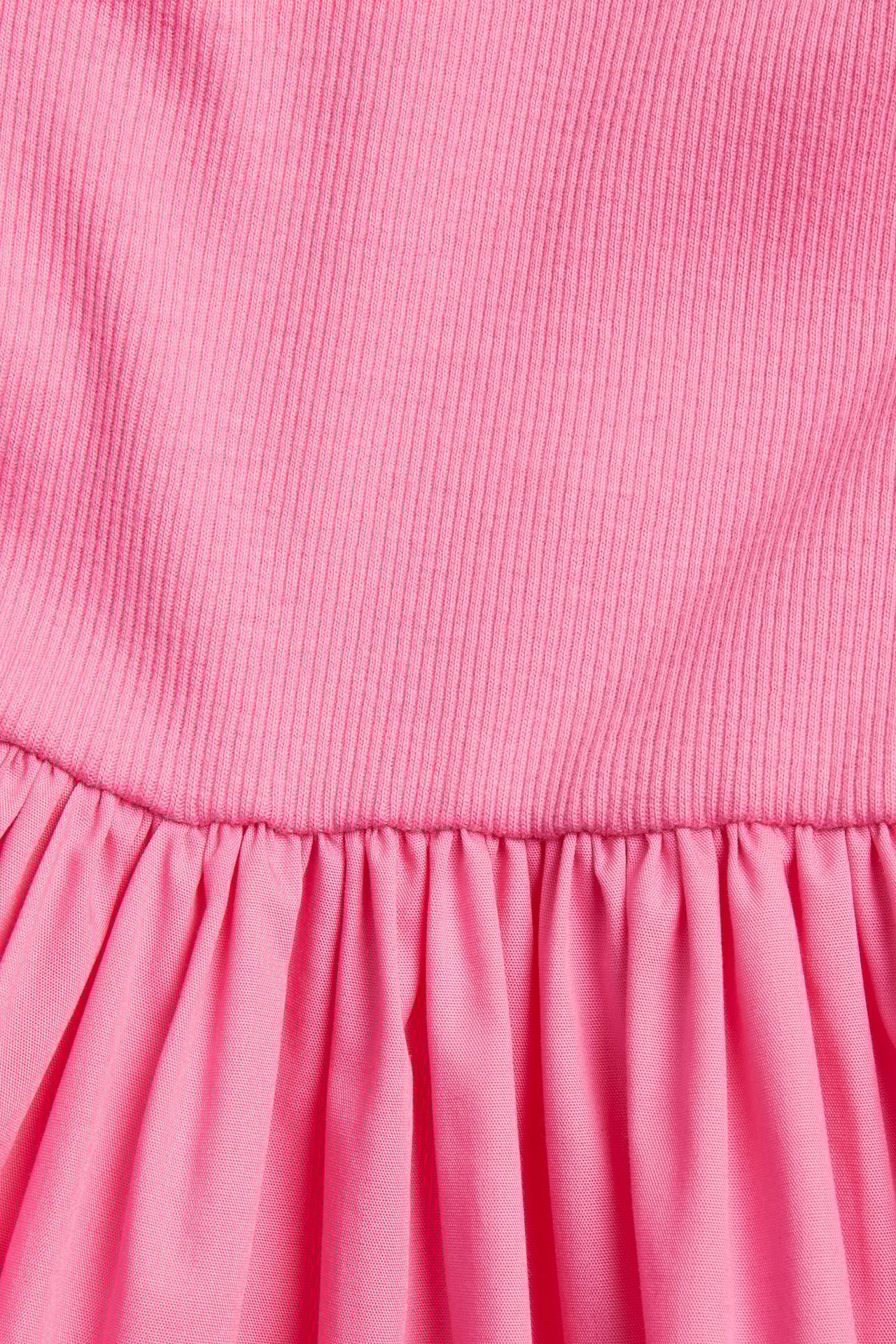 Zbliżenie różowej sukienki bez rękawów z prążkowanym dżersejowym topem i marszczoną bawełnianą spódnicą.