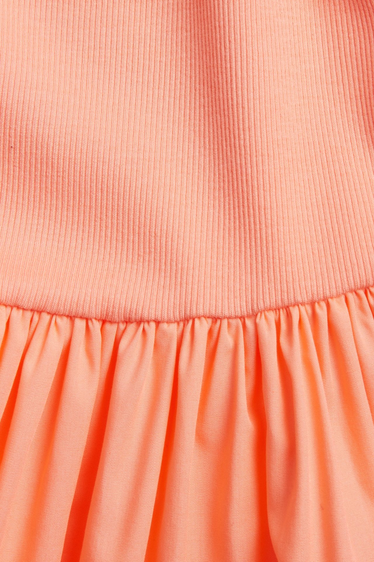 Zbliżenie na jasnopomarańczową bawełnianą sukienkę z prążkowaną górą z dżerseju i marszczoną spódnicą.