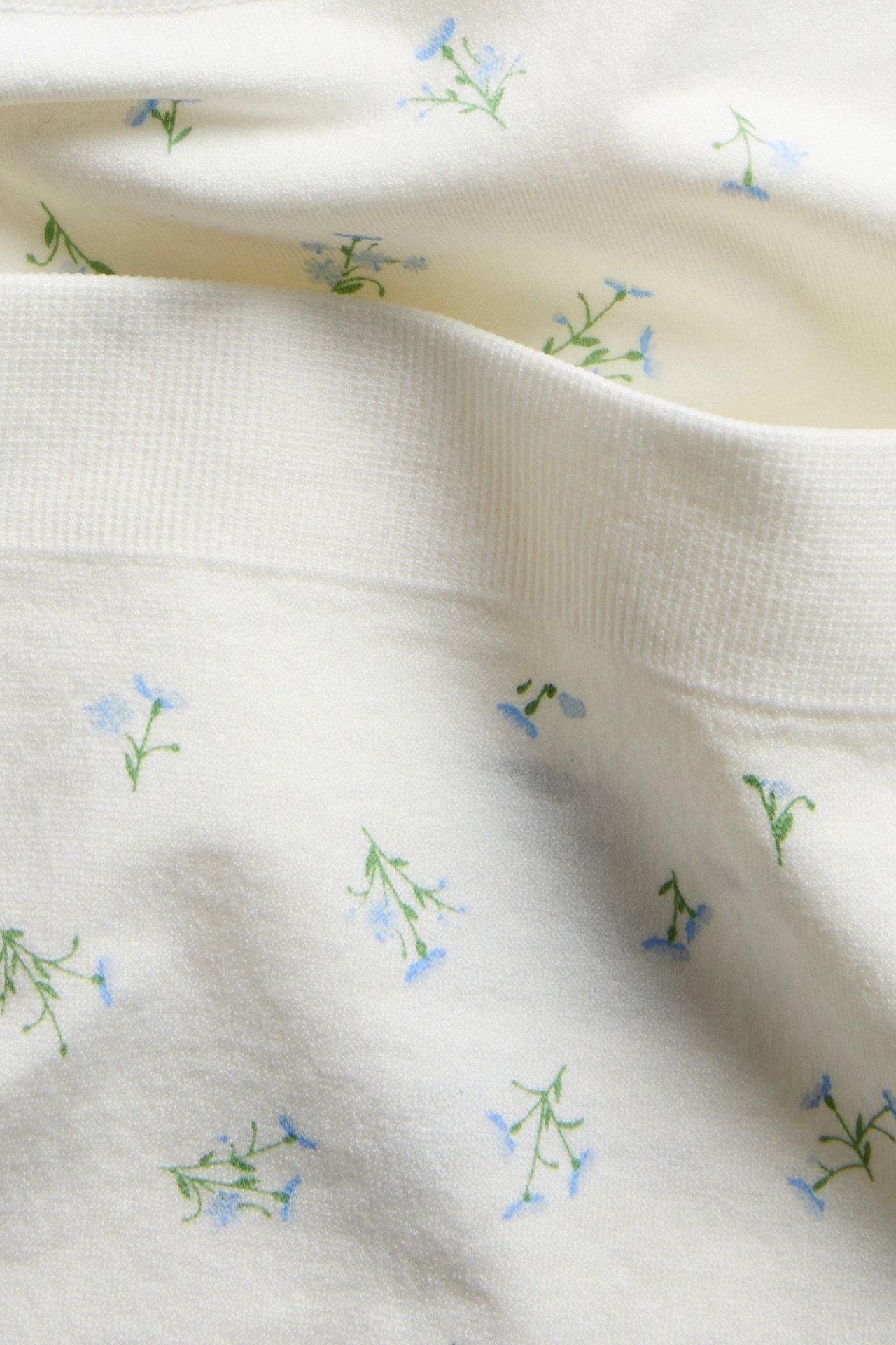 Lähikuva valkoisista brief-alushousuista, joissa ribattu vyötärö ja sininen kukkakuvio.