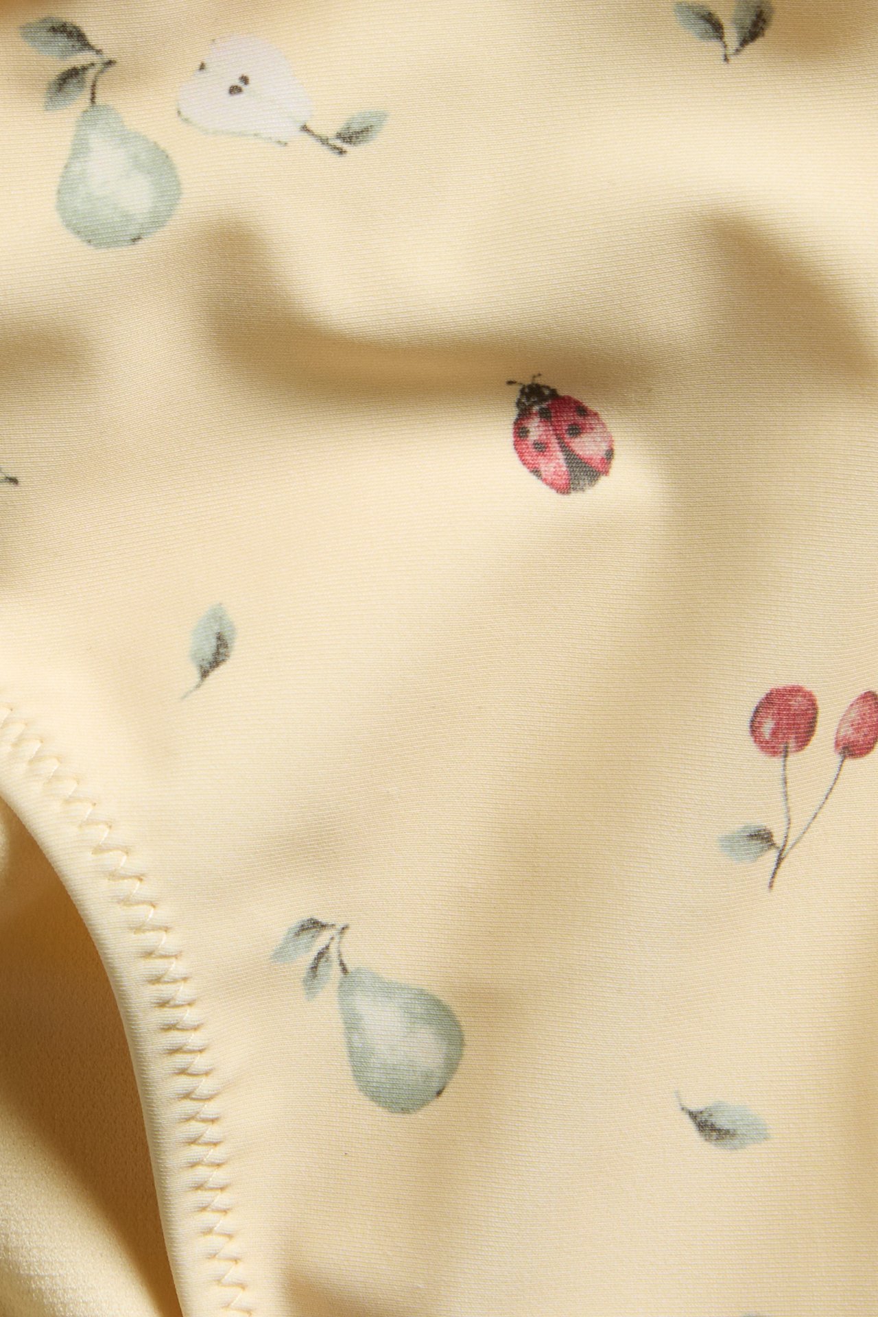 Nærbilde av gulmønstret bikinibukse med grønne pærer, røde marihøner og kirsebær.