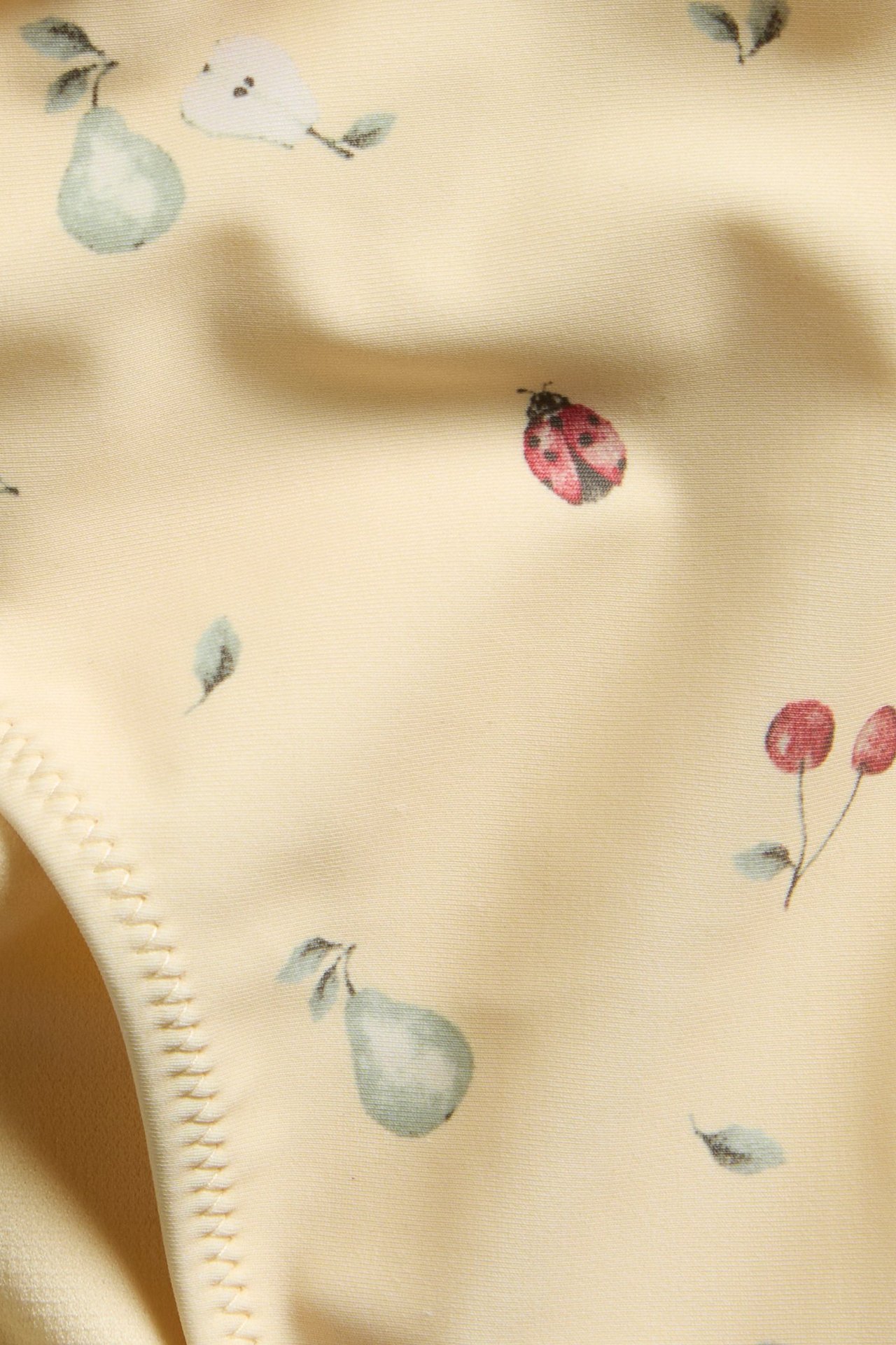 Nærbilde av gulmønstret bikinibukse med grønne pærer, røde marihøner og kirsebær.