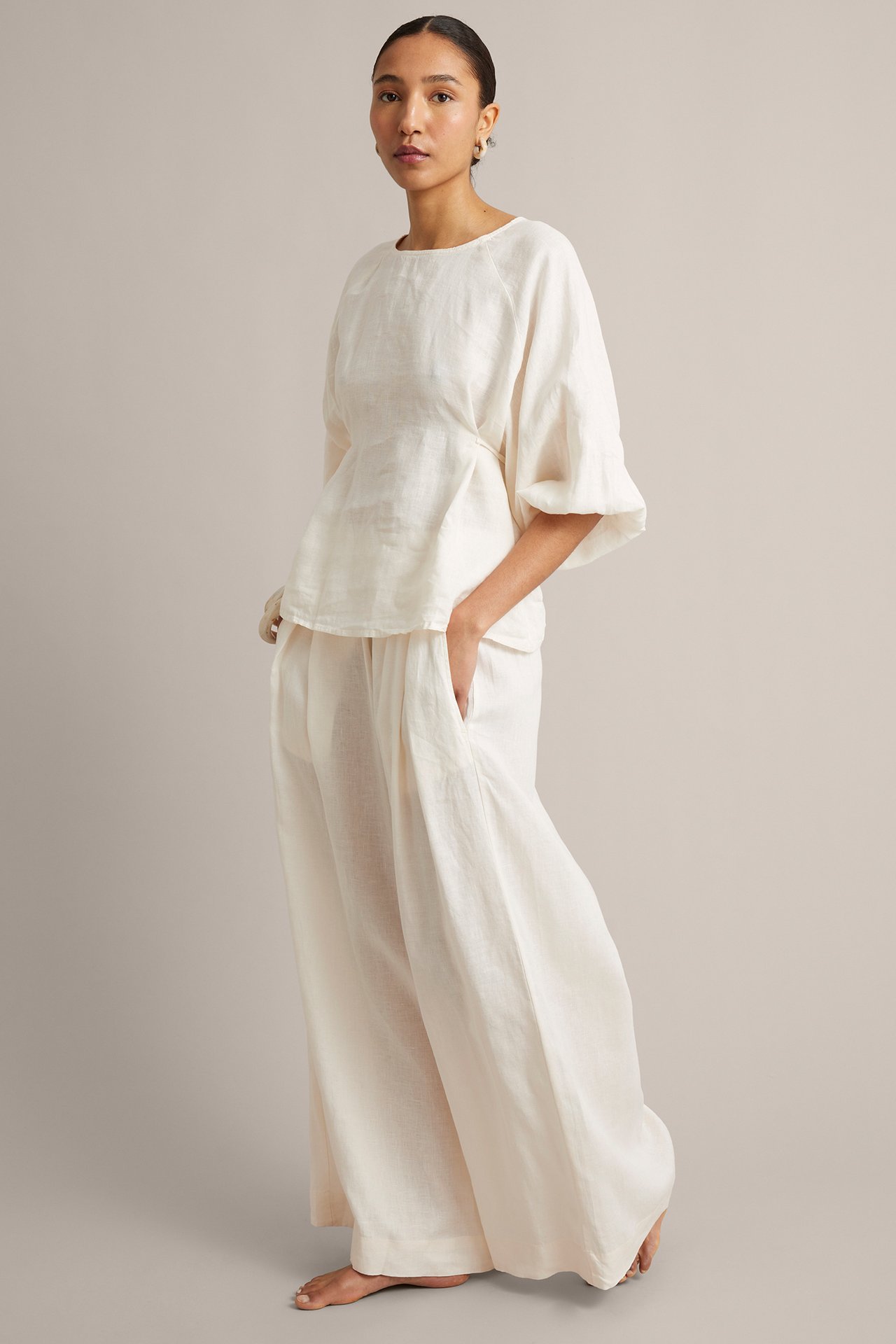 Framsida av kvinna i vita vida linnebyxor med sidfickor och matchande linnetopp.