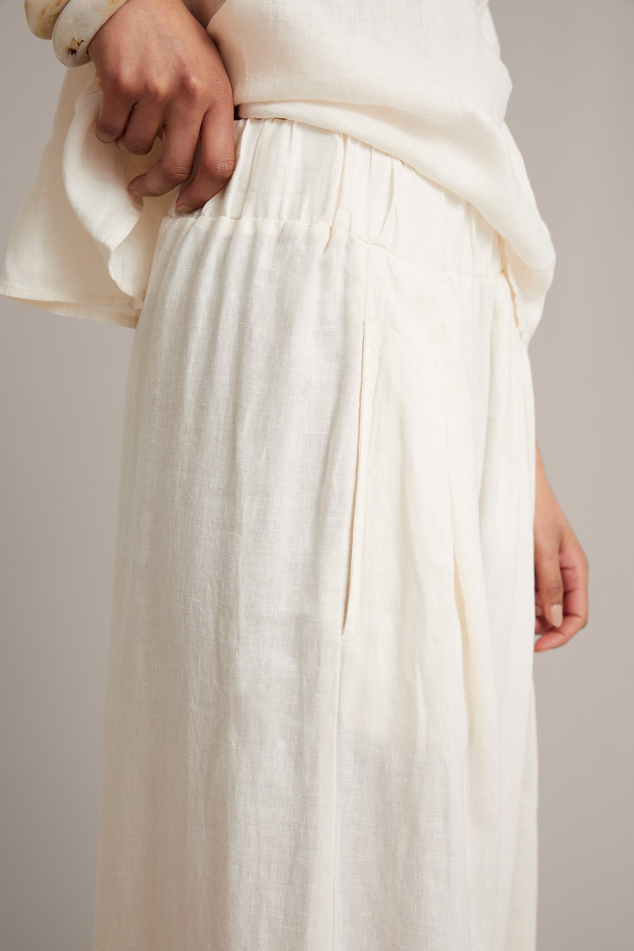 Sidovy: Kvinna i vita vida linnebyxor med elastisk midja och sidfickor, plus en matchande vit topp och armband.