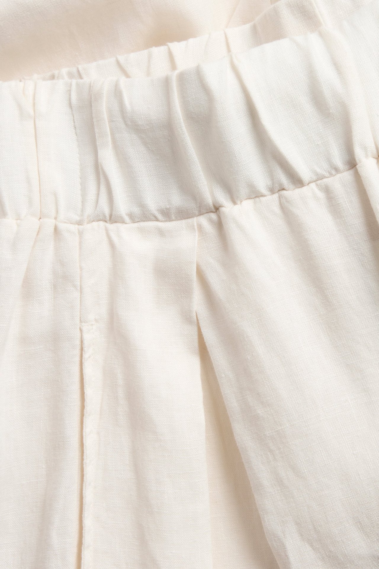 Zbliżenie białych, szerokich spodni lnianych z elastycznym pasem i zakładkami.