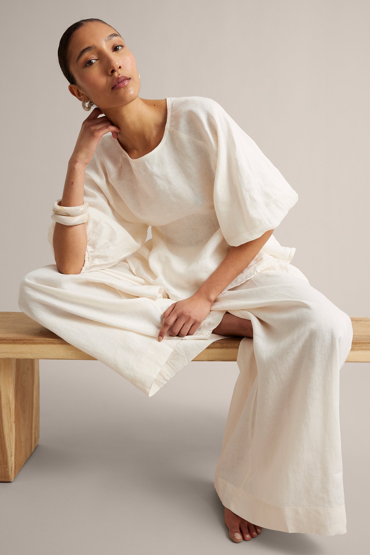 Frontvy av kvinna i vita linnebyxor med vid passform, matchande linnetopp och vita armringar.