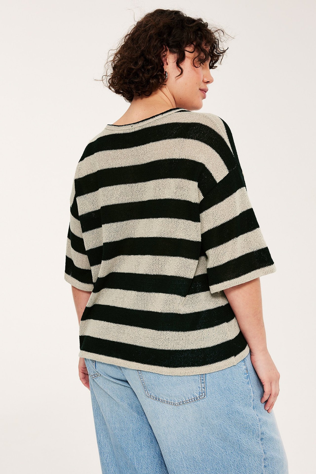 Side- og bakfra-visning av en kvinne i en svart-beige stripet kortermet strikket genser og lyseblå jeans.
