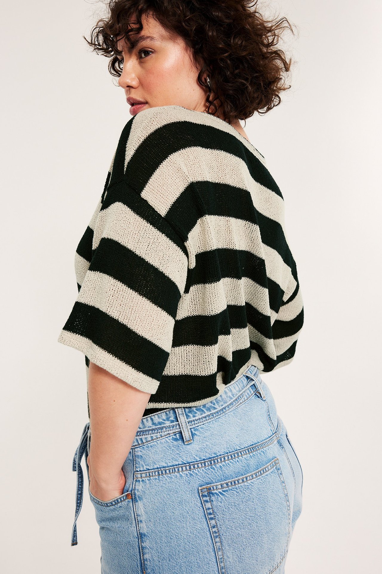 Widok z tyłu kobiety w luźnym czarno-ecru swetrze w paski z krótkim rękawem i jasnoniebieskich dżinsach.