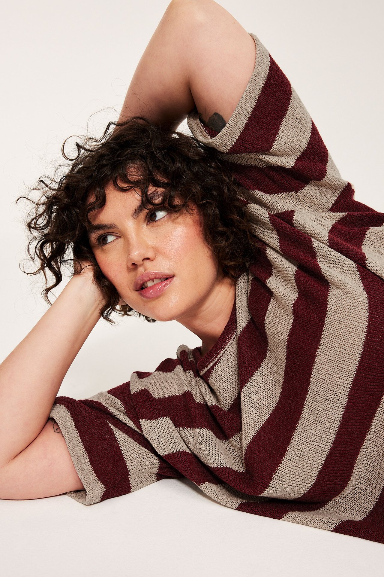 Zbliżenie kobiety w cienkim, czerwono-beżowym swetrze w paski z krótkim rękawem.